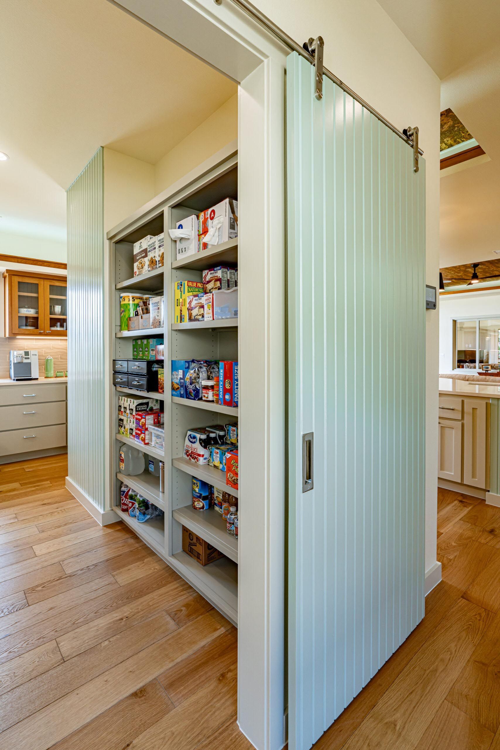 Large pantry with light blue sliding barn doors, filled with food items on shelves.