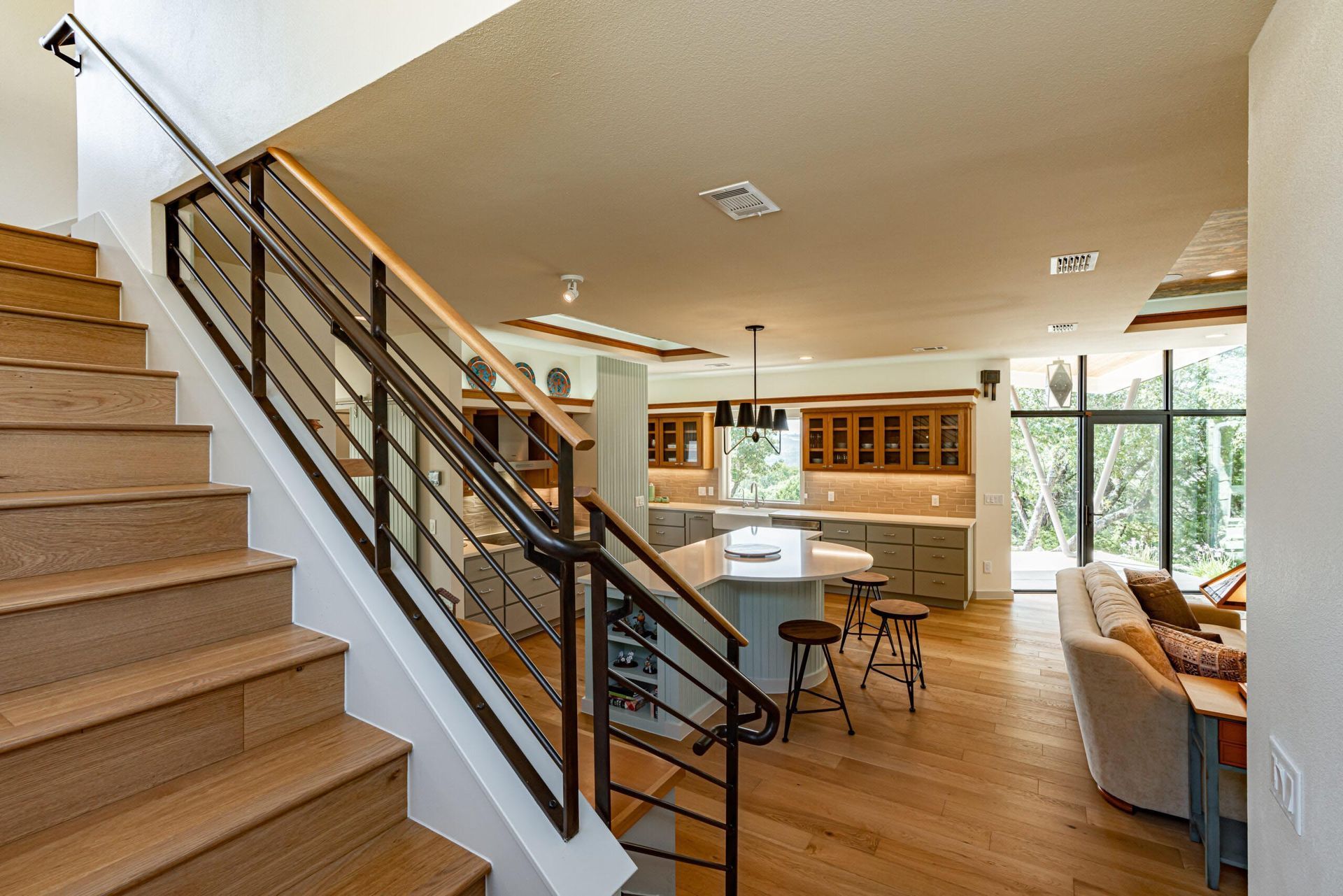 Wooden staircase leads into an open-plan kitchen and living room with large windows, wood floors, and modern furnishings.