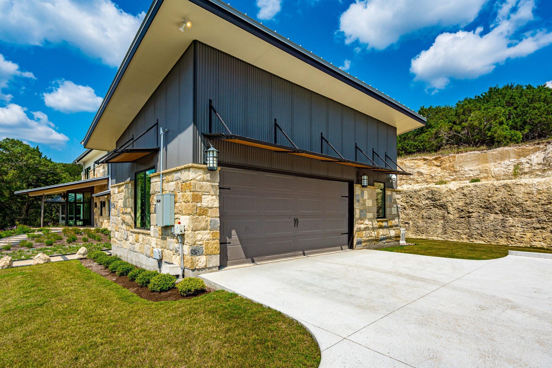 Modern home with stone and metal siding, a driveway, and garage.