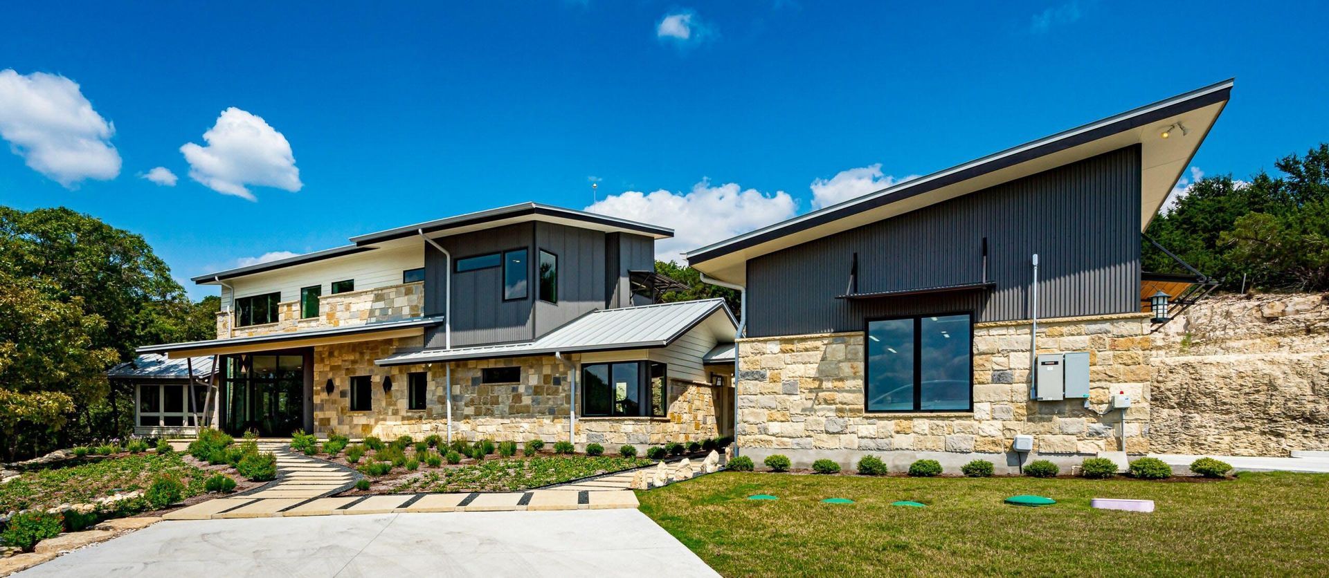 Modern home with stone facade and angled roof, set against a bright blue sky.