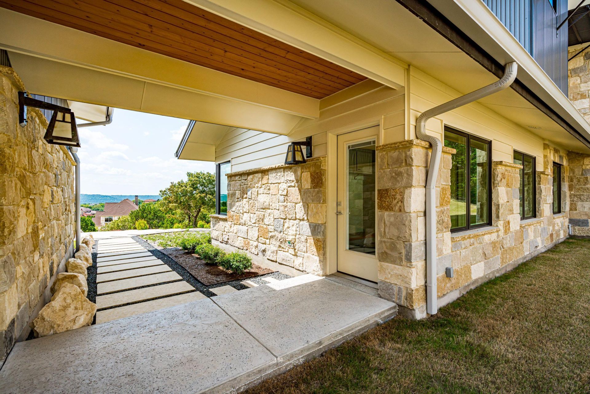 Stone home exterior with covered walkway, view of landscaped path, and a distant vista.