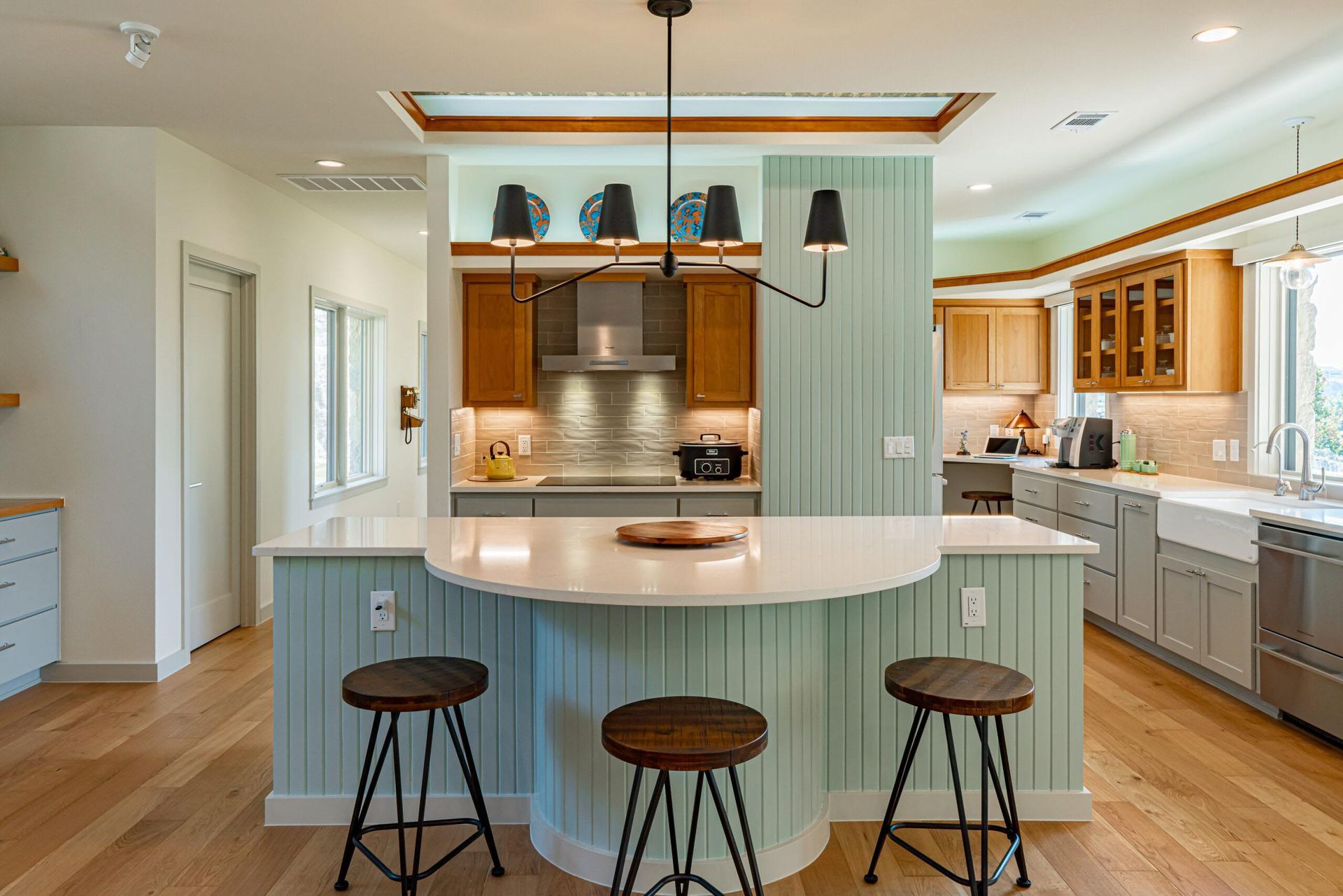 A modern kitchen with a light blue island, three stools, and wooden cabinets.