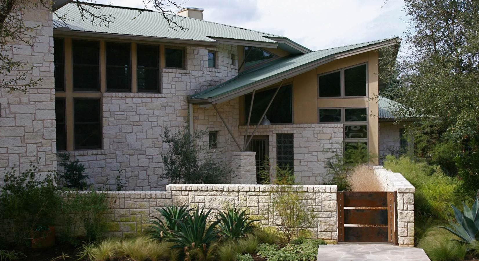 Stone house with green roof and a wooden gate in front.