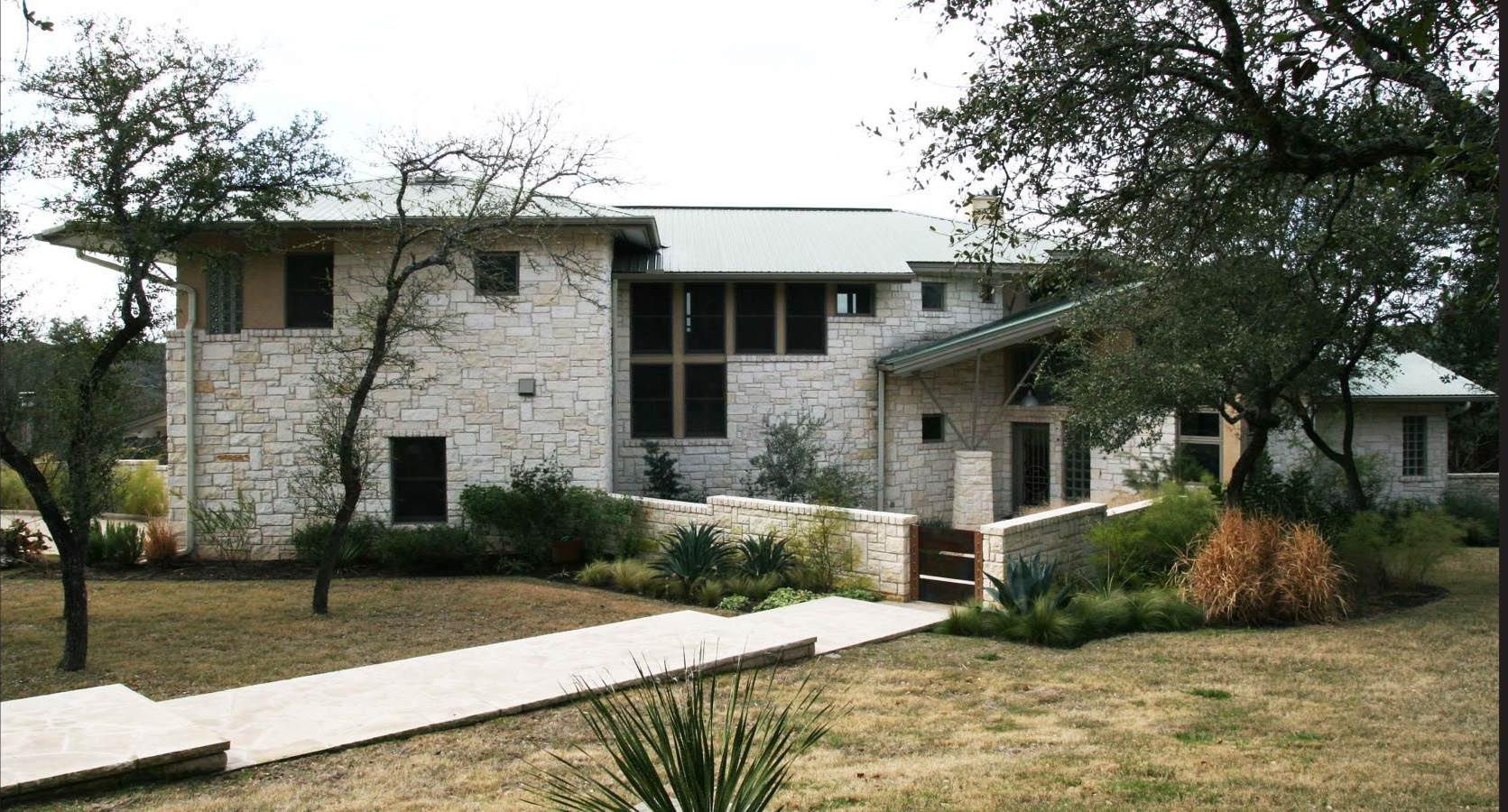 Two-story stone house with a walkway leading to the entrance, trees, and landscaping.