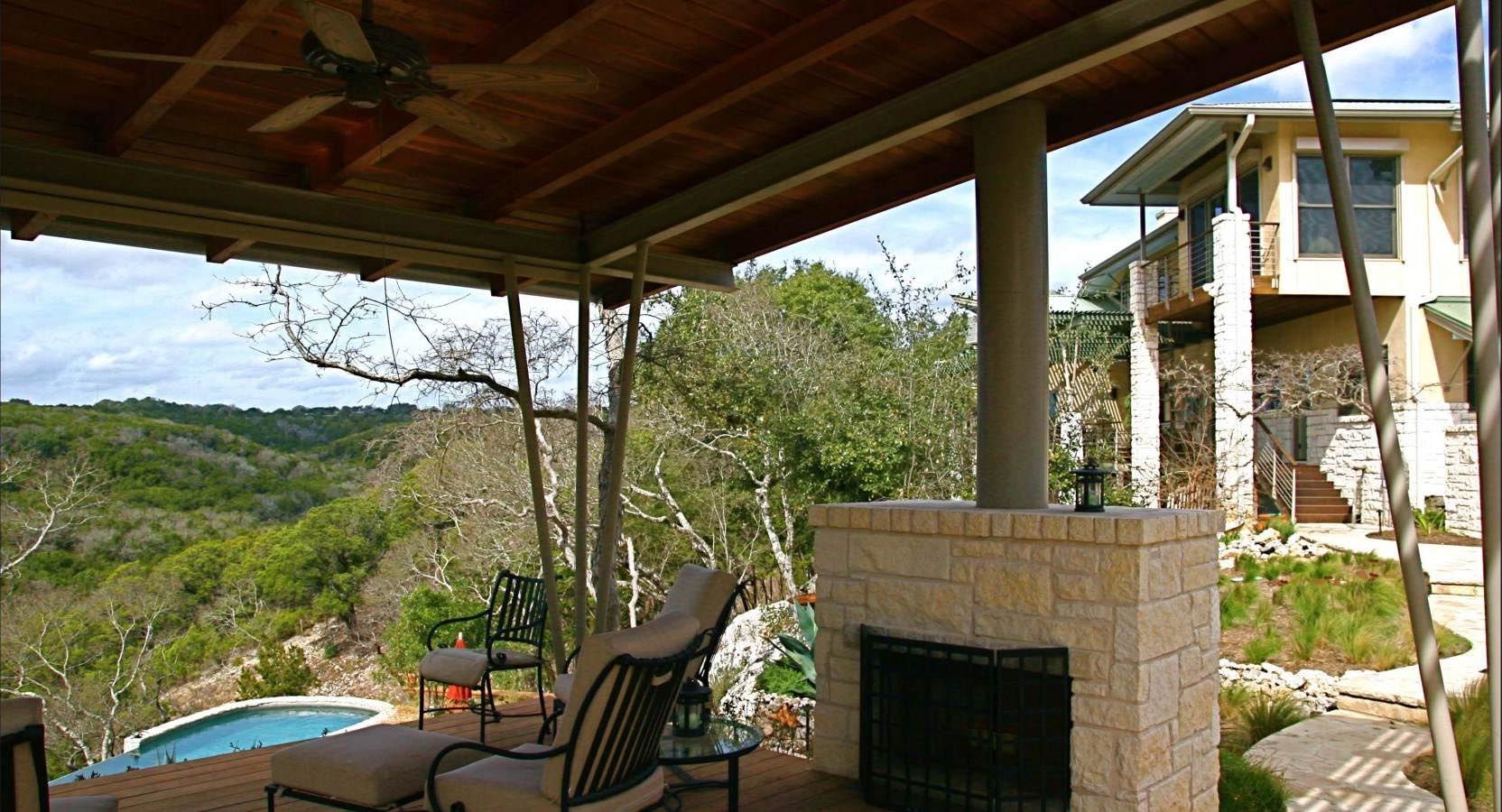 Patio with fireplace overlooking a pool and rolling hills, part of a multi-story home.