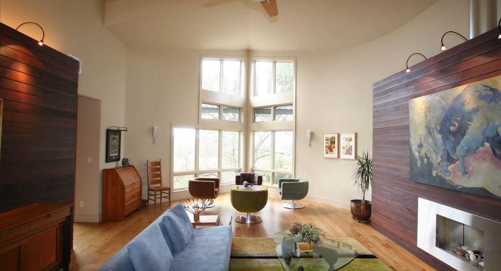 Spacious living room with large windows, light wood floors, blue sofa, and modern furniture.