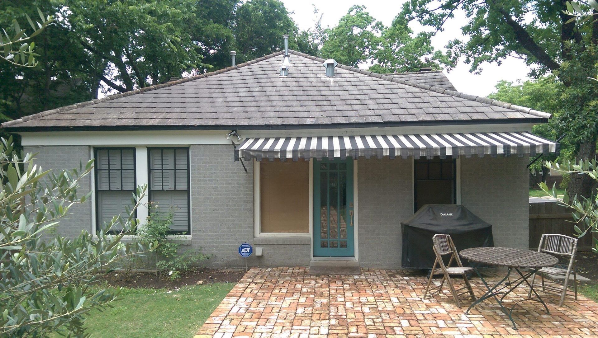 Small gray house with brick patio, awning, and outdoor furniture.