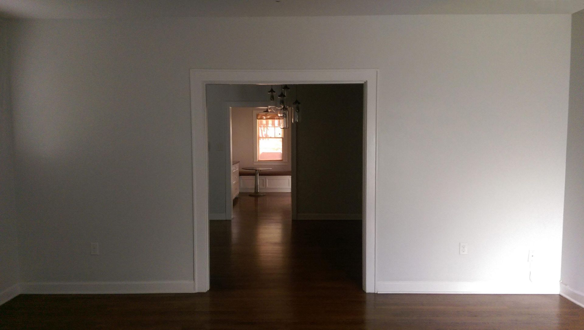 Interior view of a room with an open doorway leading to another room; white walls and dark wood floor.