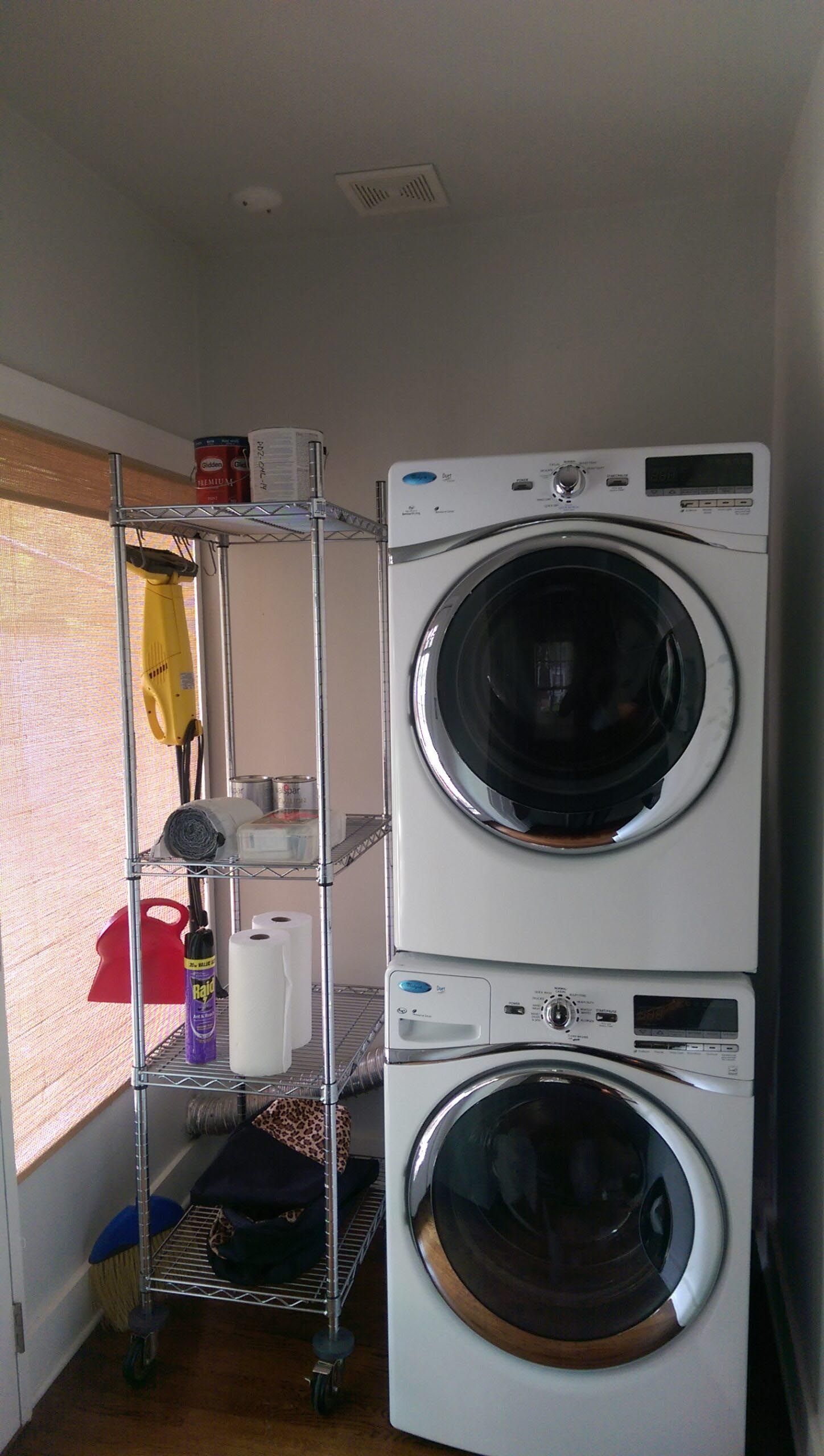 Stacked white washer and dryer with a chrome shelving unit in a laundry room.