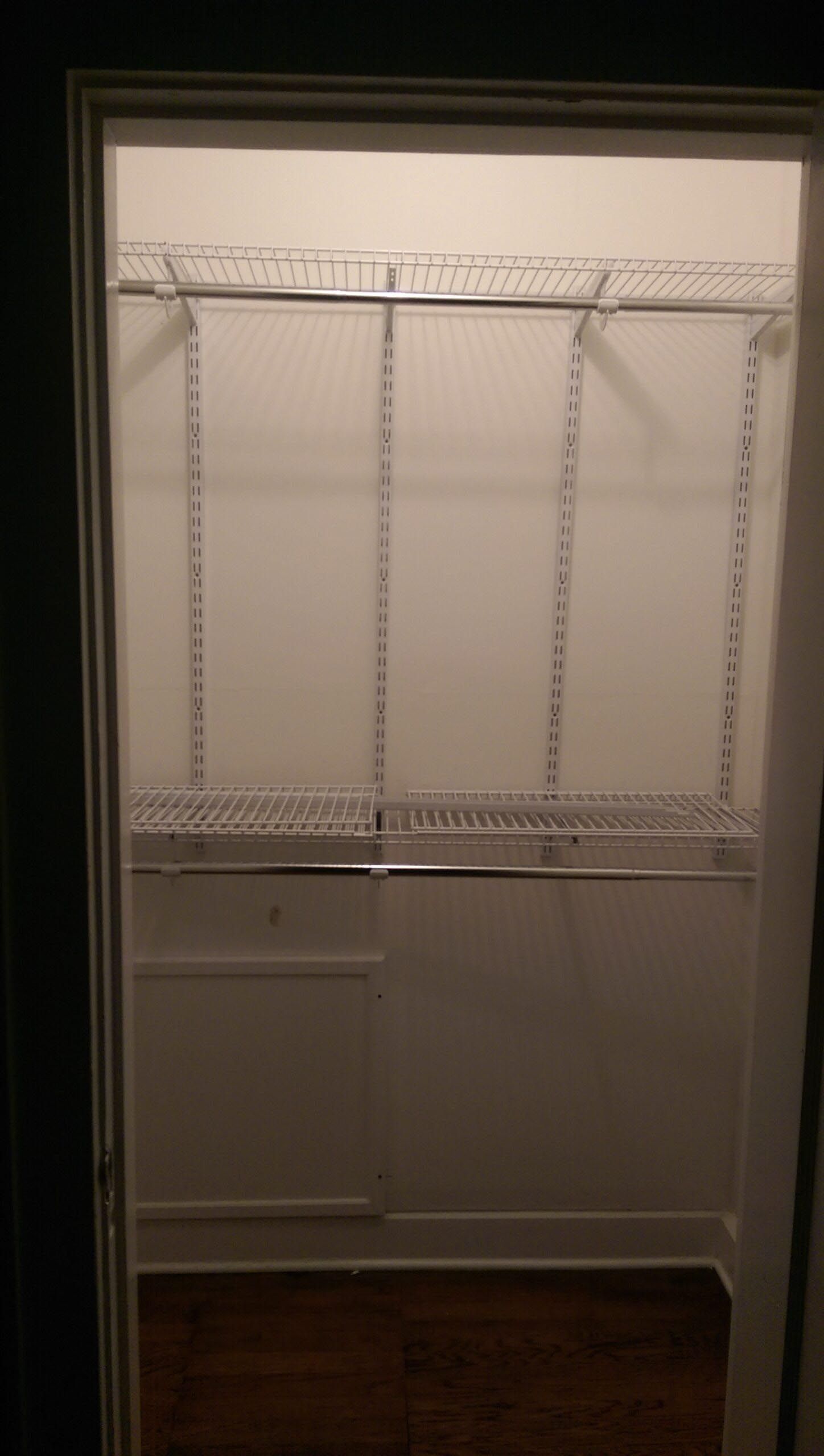 White closet interior with shelves and a hanging rod, viewed from the doorway. Dark wood floor.