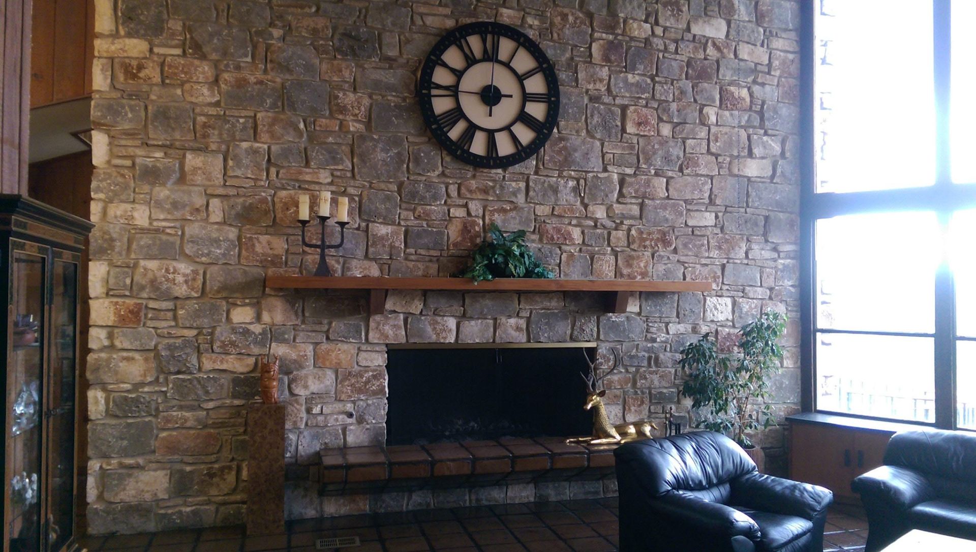 Stone fireplace with clock and mantle; black leather chairs sit nearby.