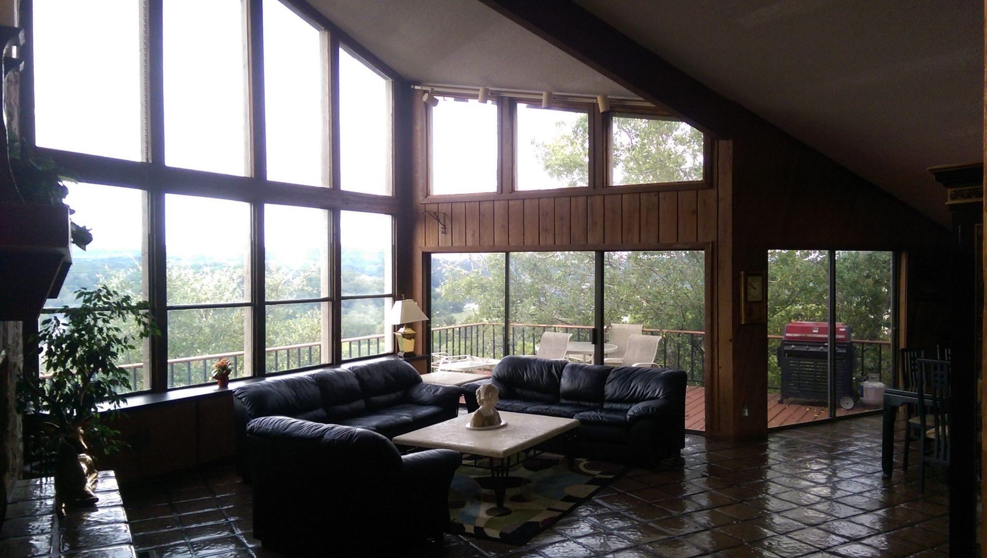 Living room with large windows overlooking a green landscape, two black leather sofas, and a stone fireplace.