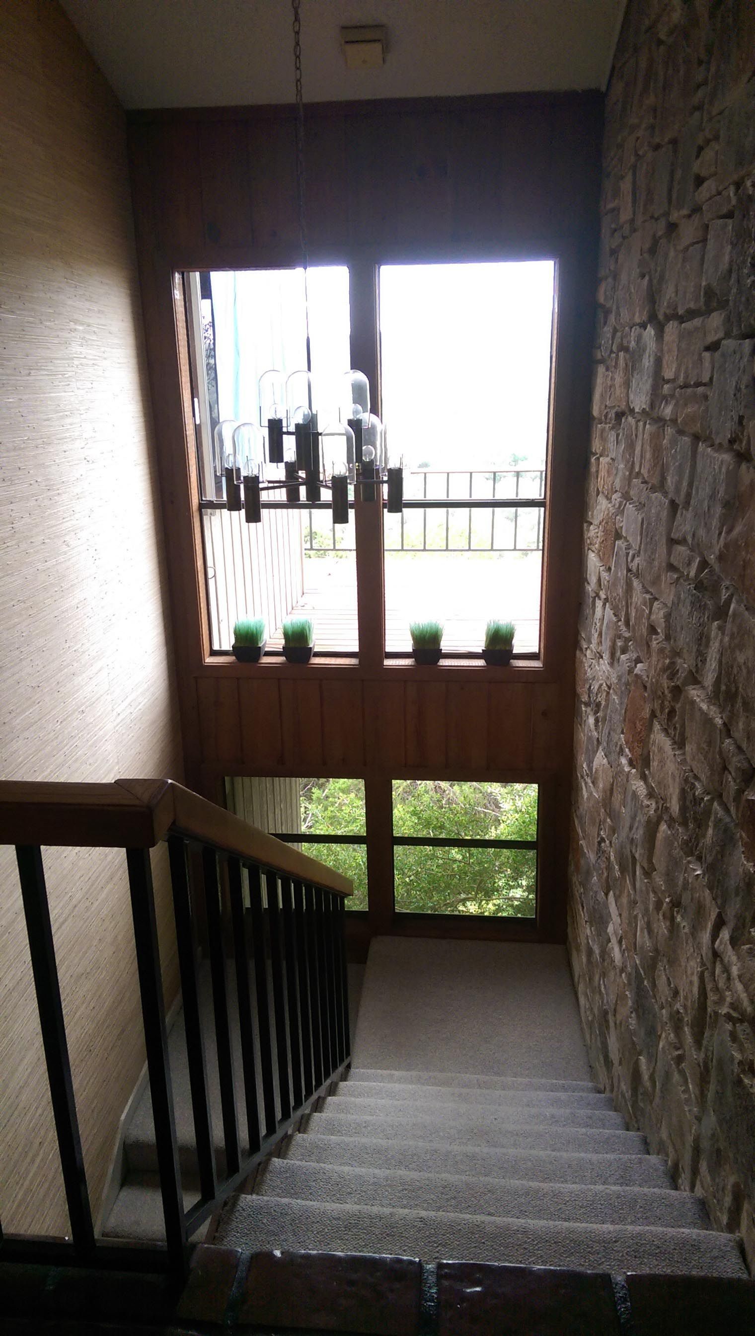 Staircase with wooden railing and stone wall. Window at top of stairs.