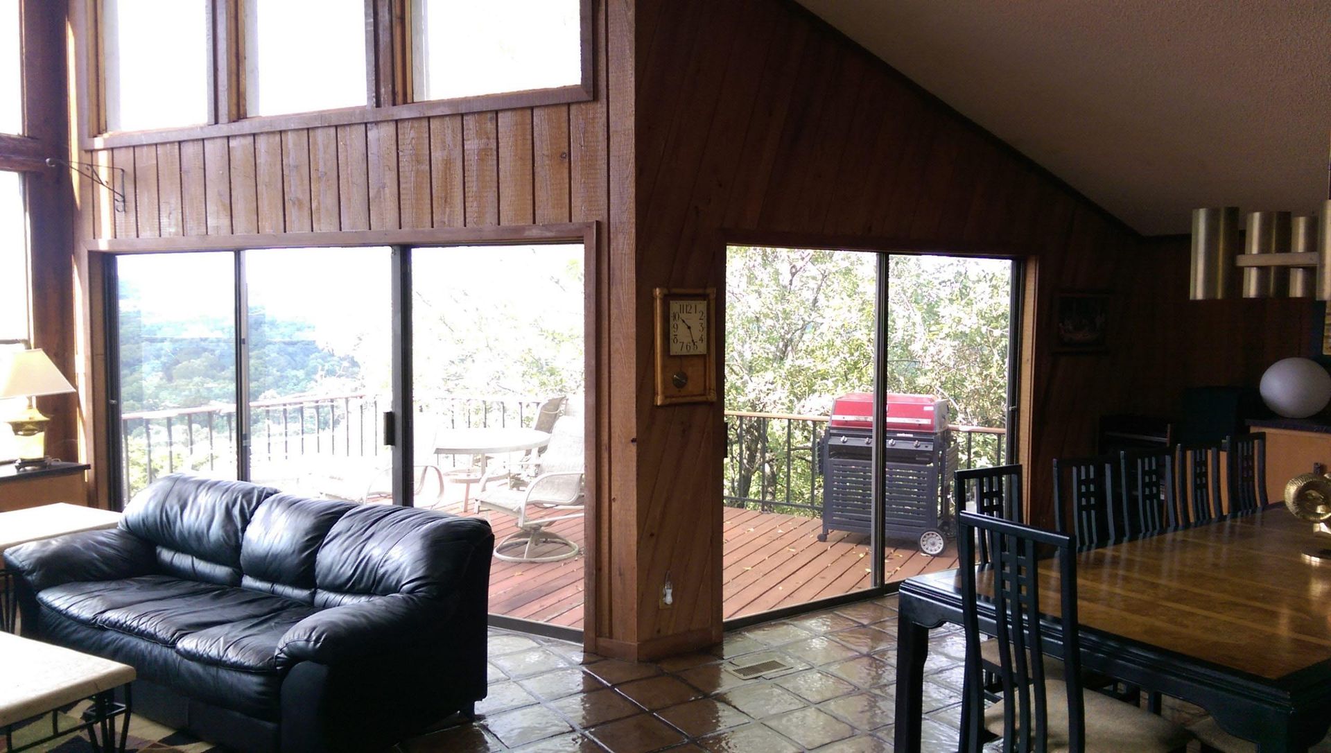 Interior view of a living room with a black leather couch, sliding glass doors to a deck, and a dining area.