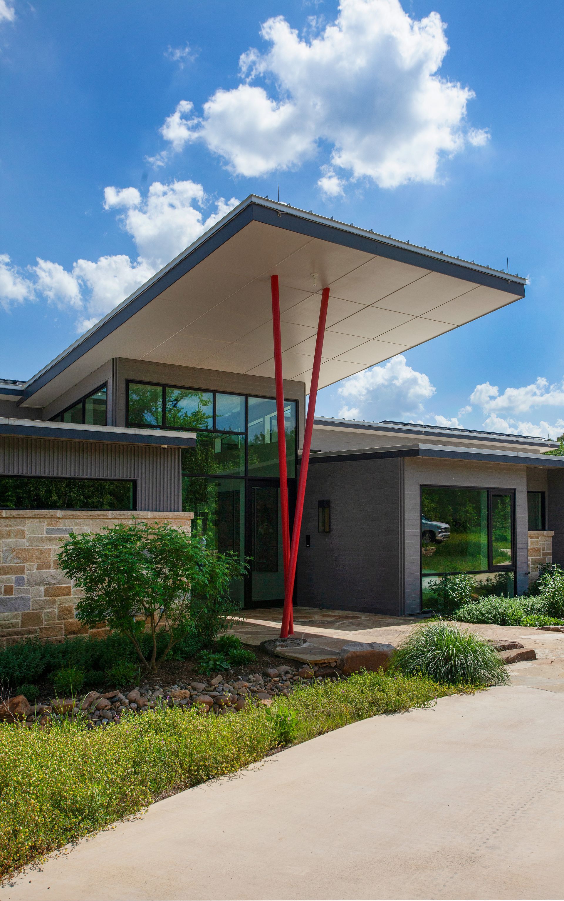 Modern home with a flat roof supported by red poles, blue sky background.