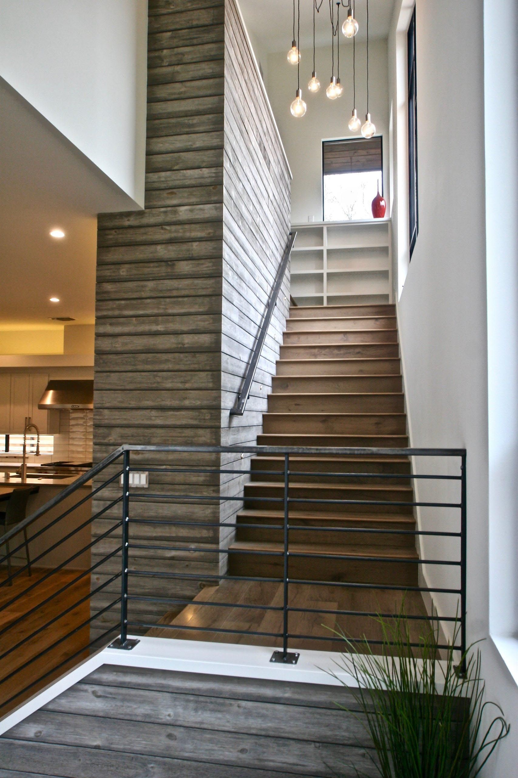 Wooden staircase with black railings and pendant lights, next to a textured wall.