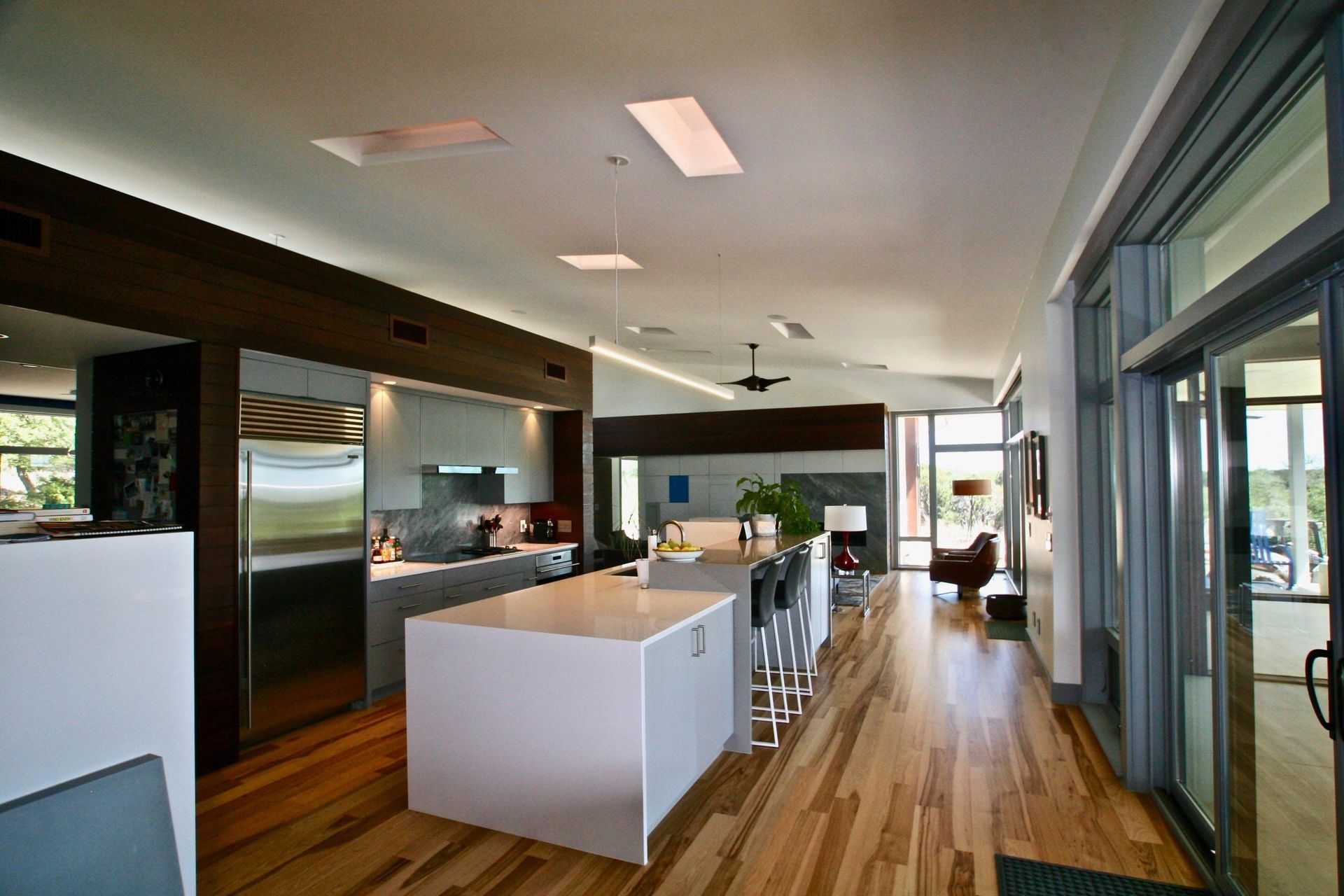 Modern kitchen with wooden floors, white island, stainless steel appliances, and large windows.