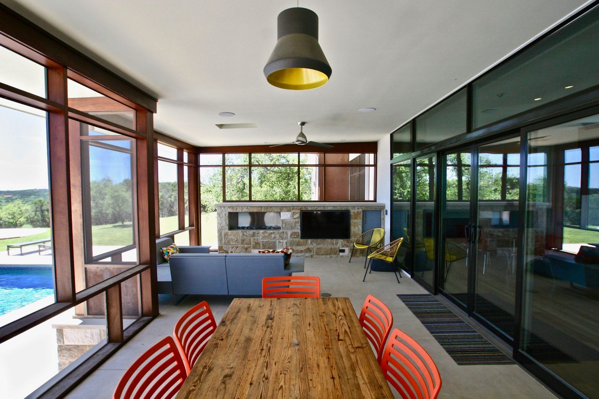 Sunroom with large windows, dining table, and pool view; orange chairs and gray sofa.