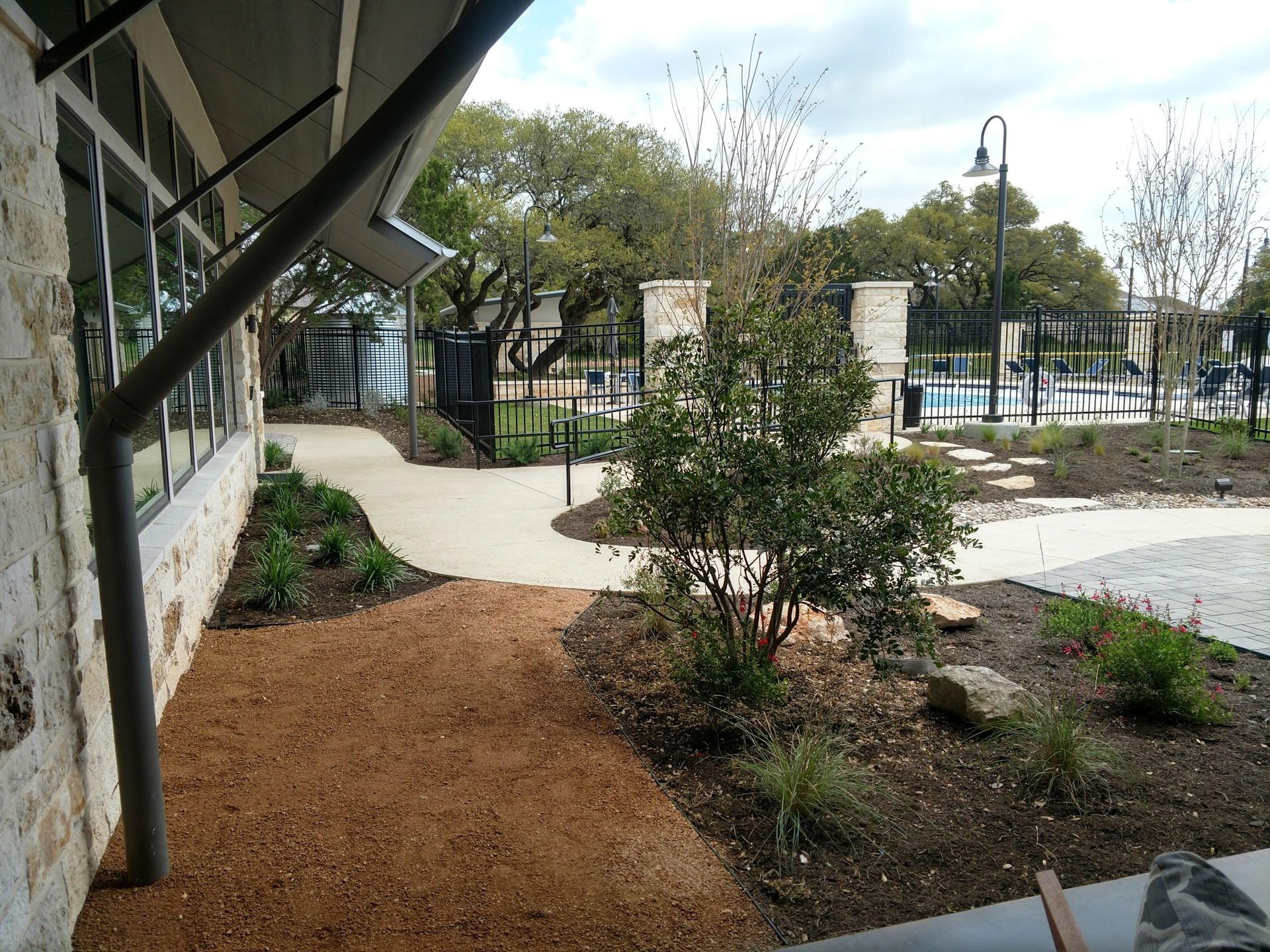 Path leading to a pool area with landscaping and building in the foreground, and a cloudy sky.