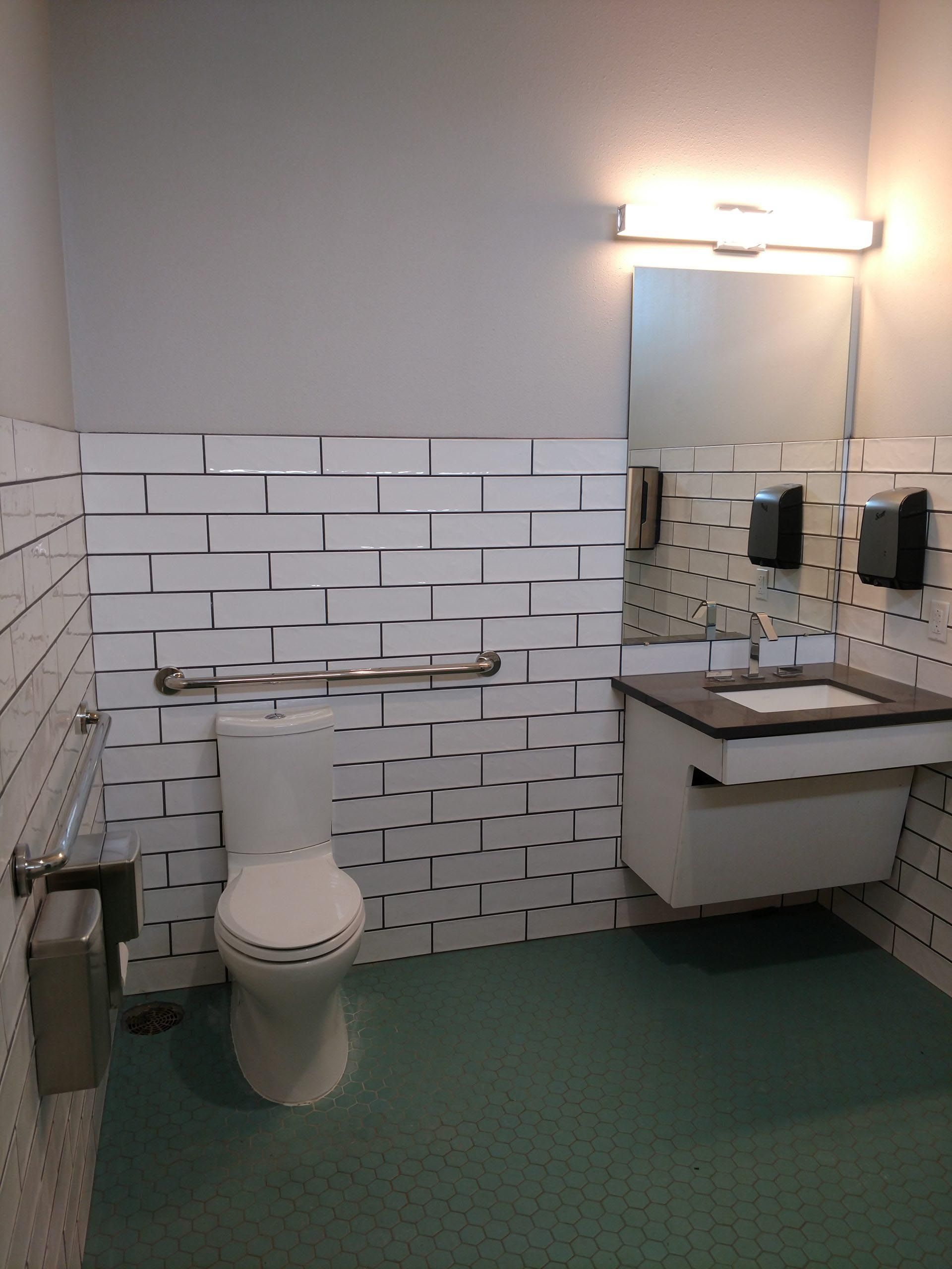 ADA-compliant public restroom with toilet, sink, grab bar, tiled walls and green floor.