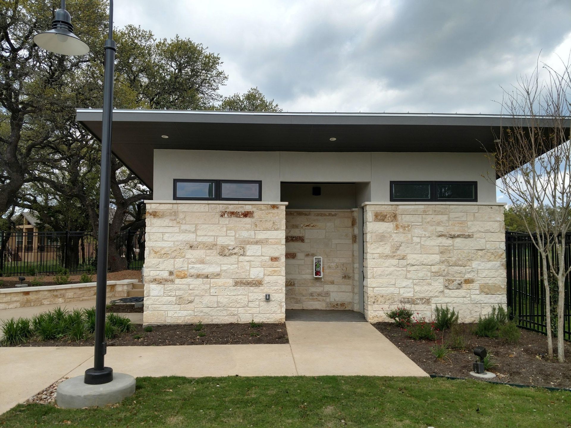 Modern public restroom building with stone facade and gray roof, in a grassy park setting.