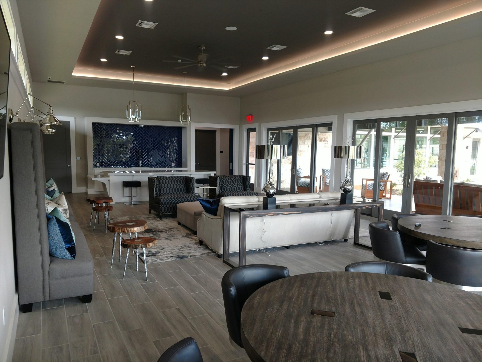 Spacious lounge with seating, round tables, and an accent wall. Large windows provide natural light.