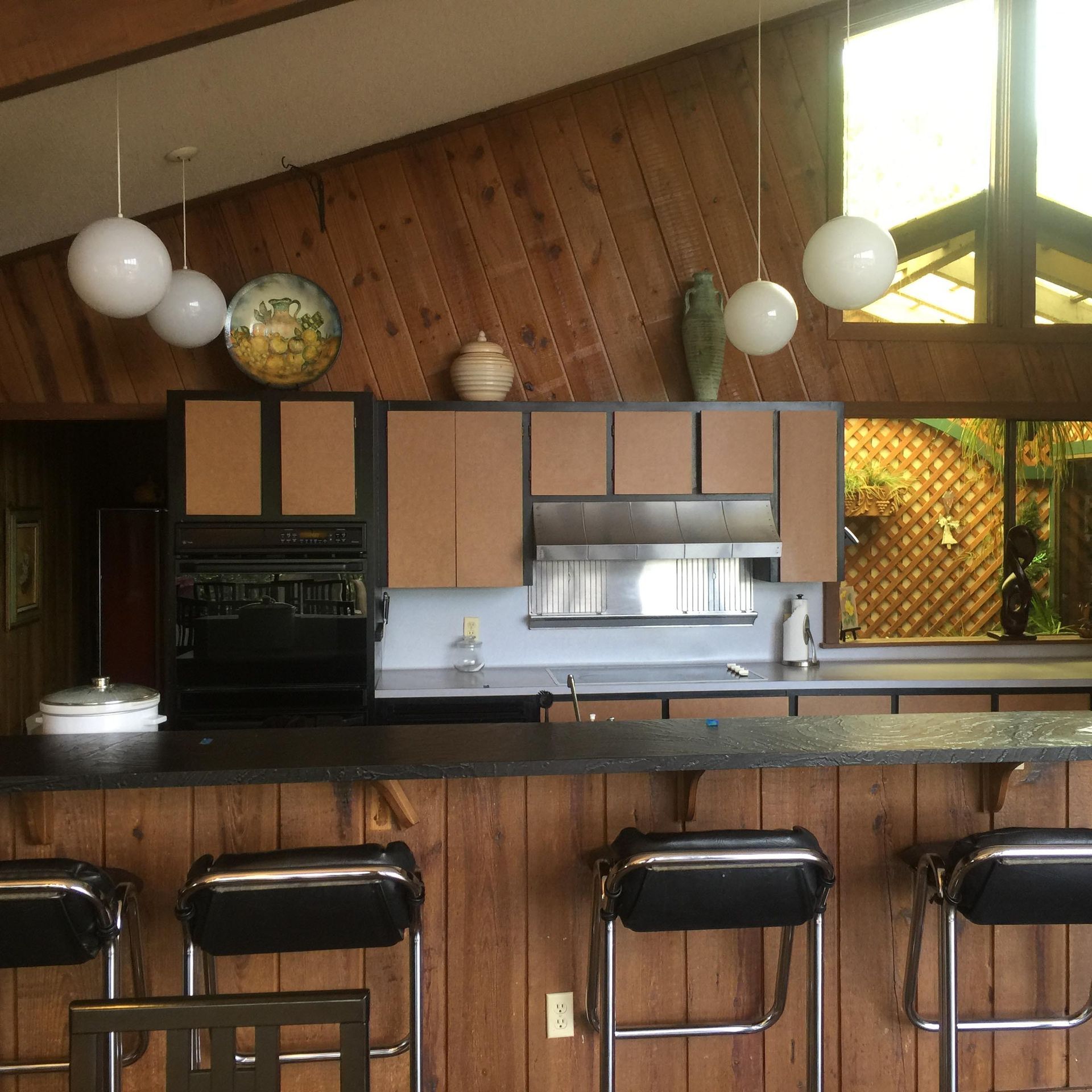 Kitchen with wood paneling, dark countertops, and globe pendant lights over a bar with stools.