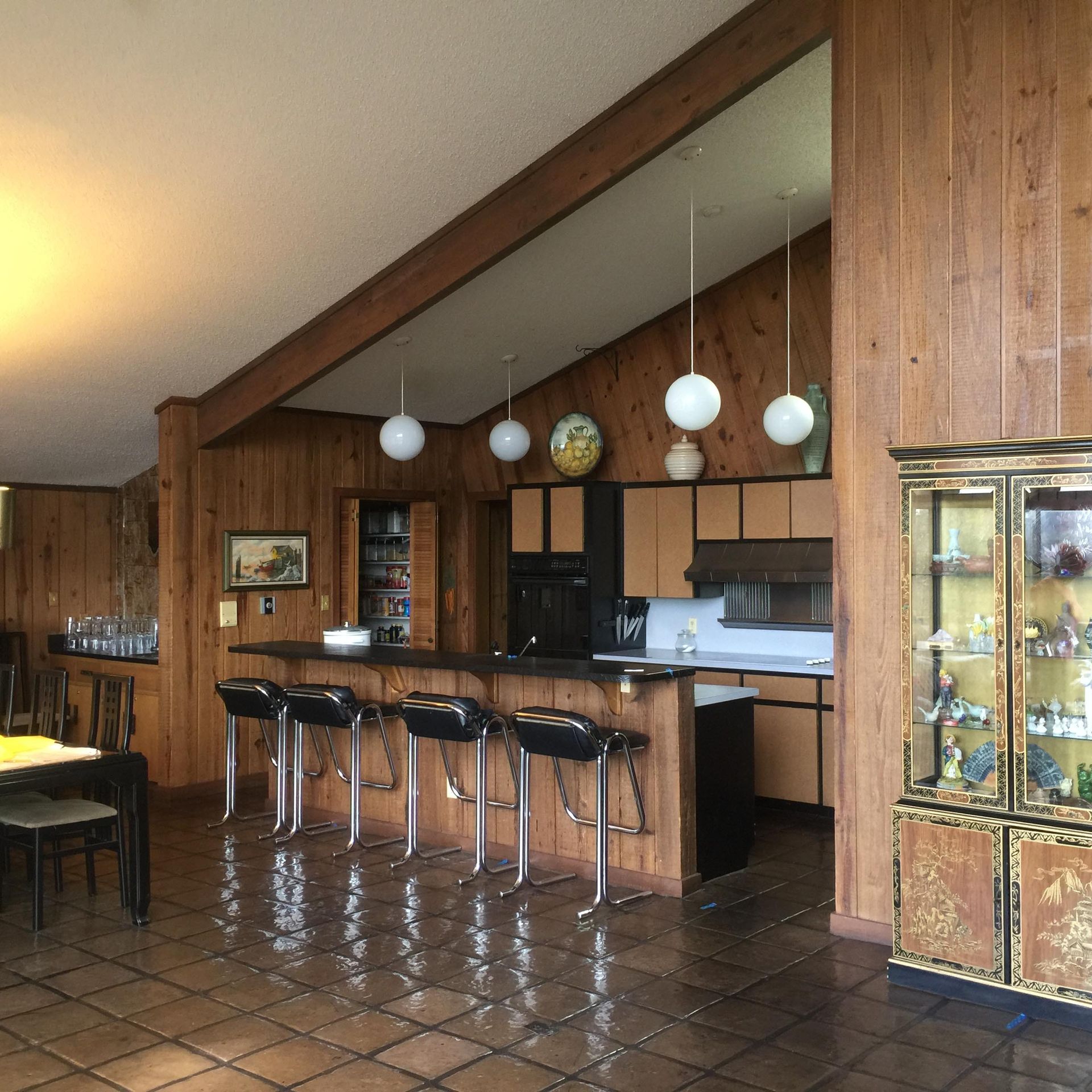 Kitchen with wood paneling, black and tan cabinets, bar stools, and globe pendant lights.