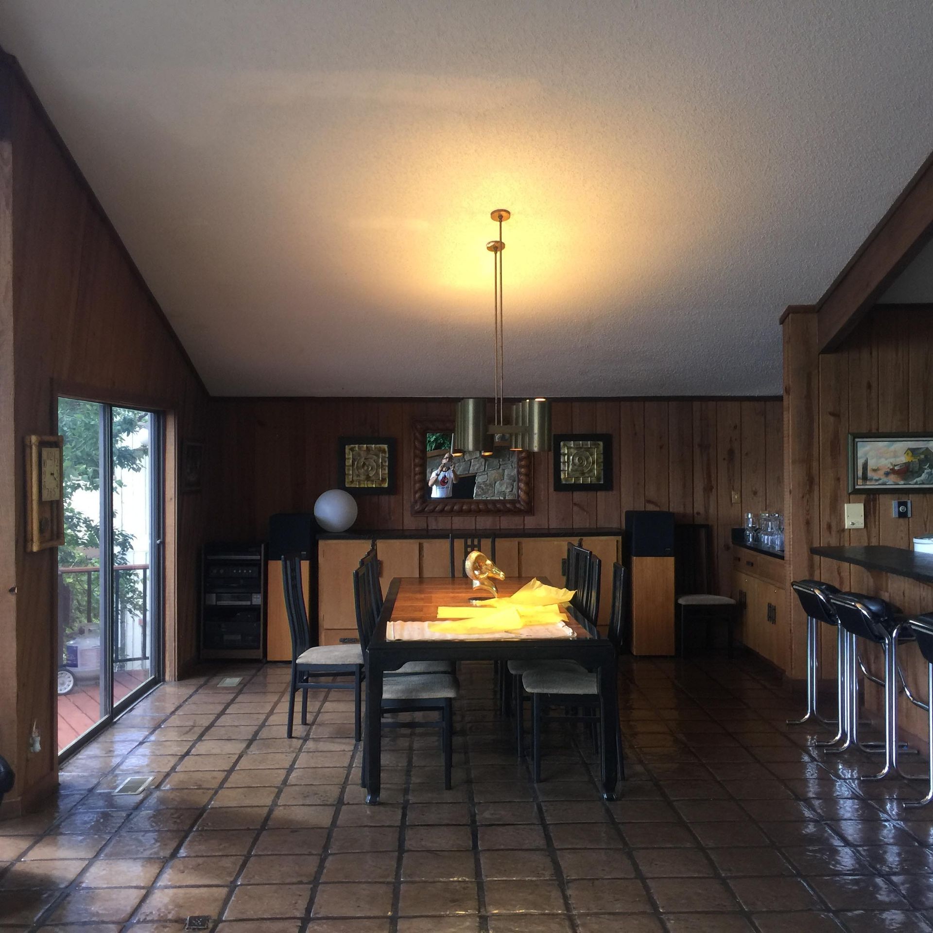 Dining room with wooden panel walls, tile floor, table with chairs, and a bar with stools.