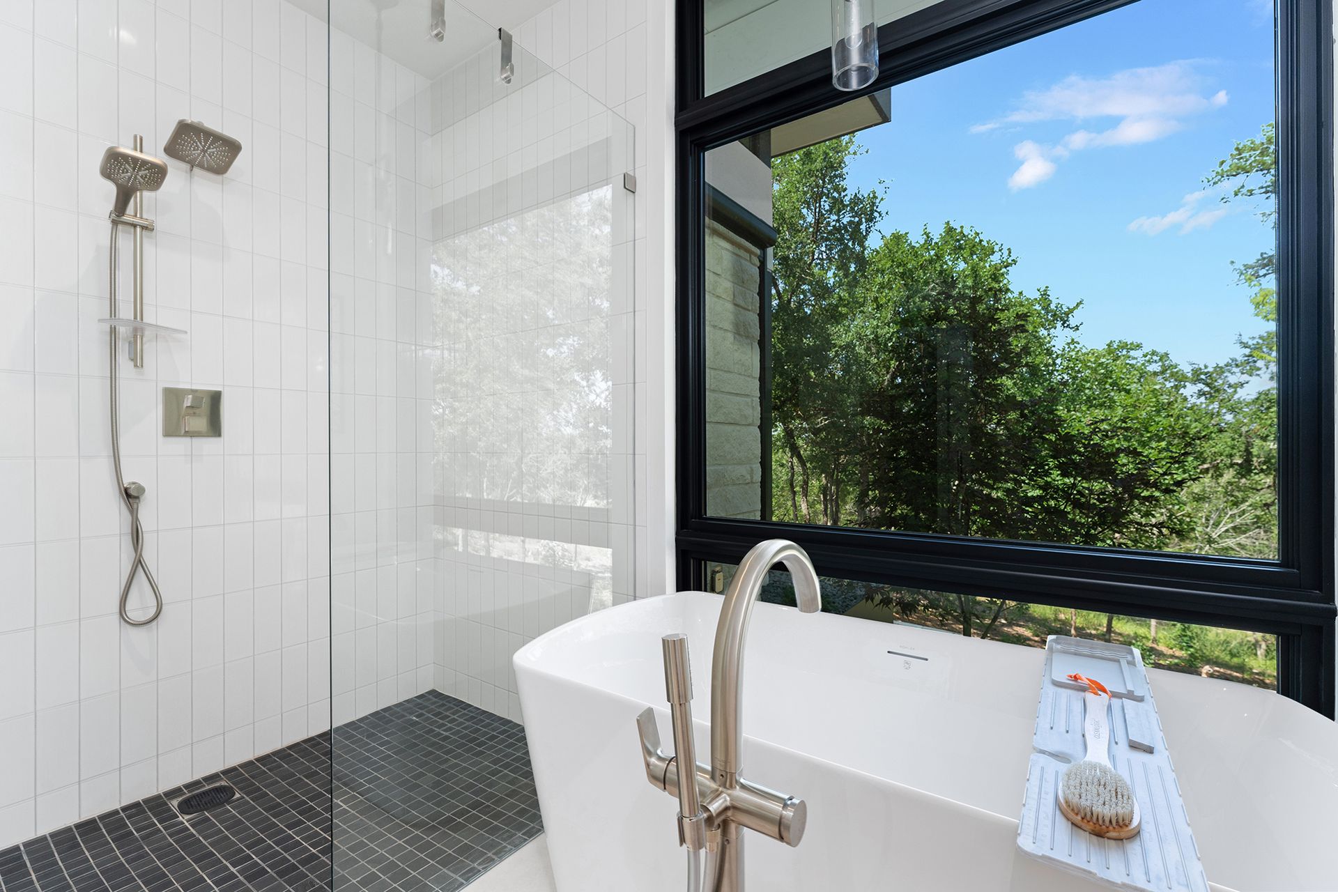Modern bathroom with a bathtub, shower, large window overlooking trees, and white and gray tiles.