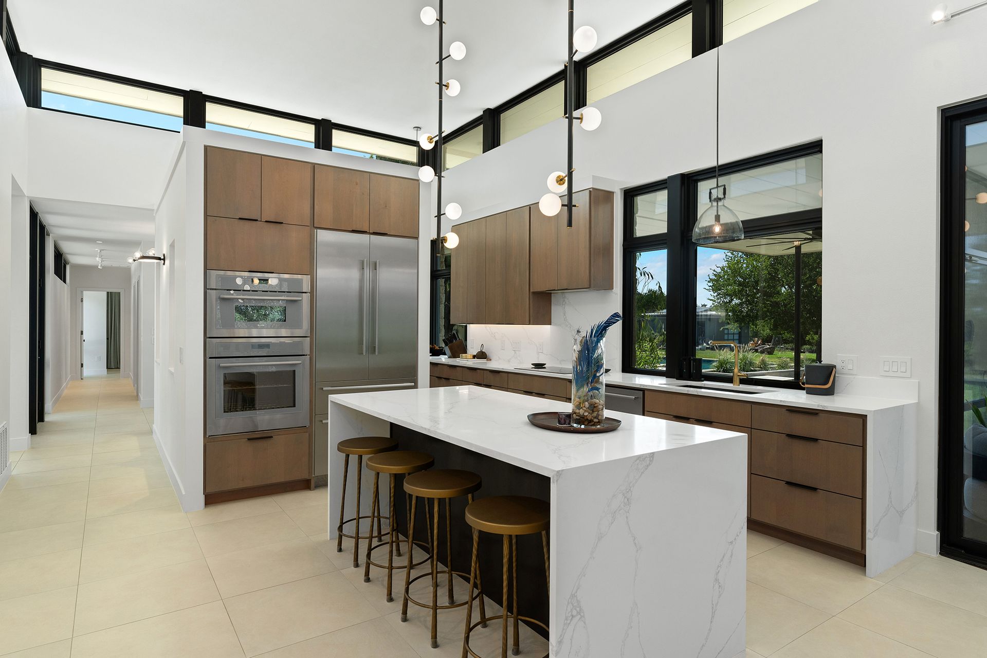 Modern kitchen with white countertops, wooden cabinets, stainless steel appliances, and a large island with bar stools.