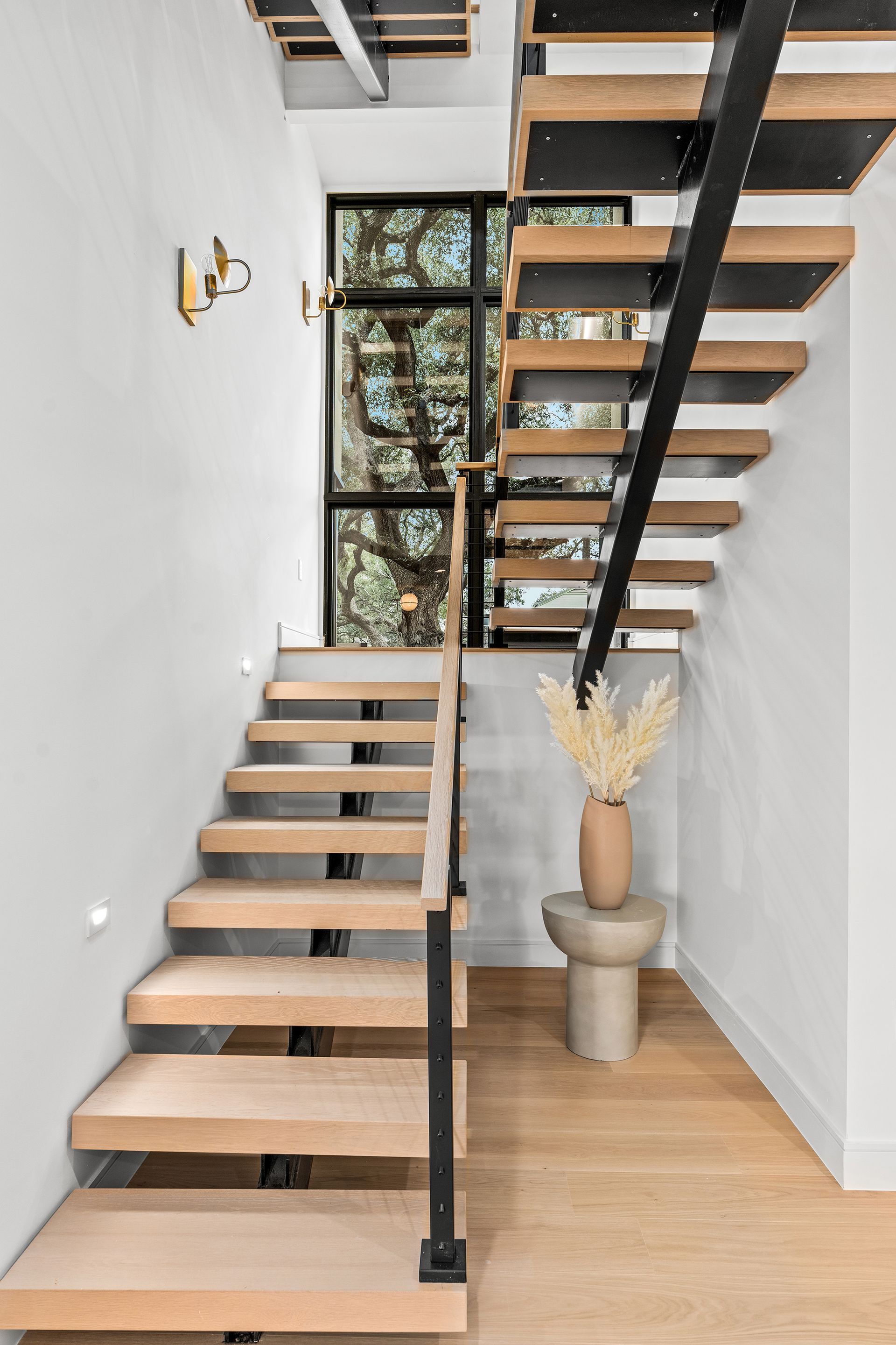 A modern staircase with wooden steps and a black railing in a hallway.