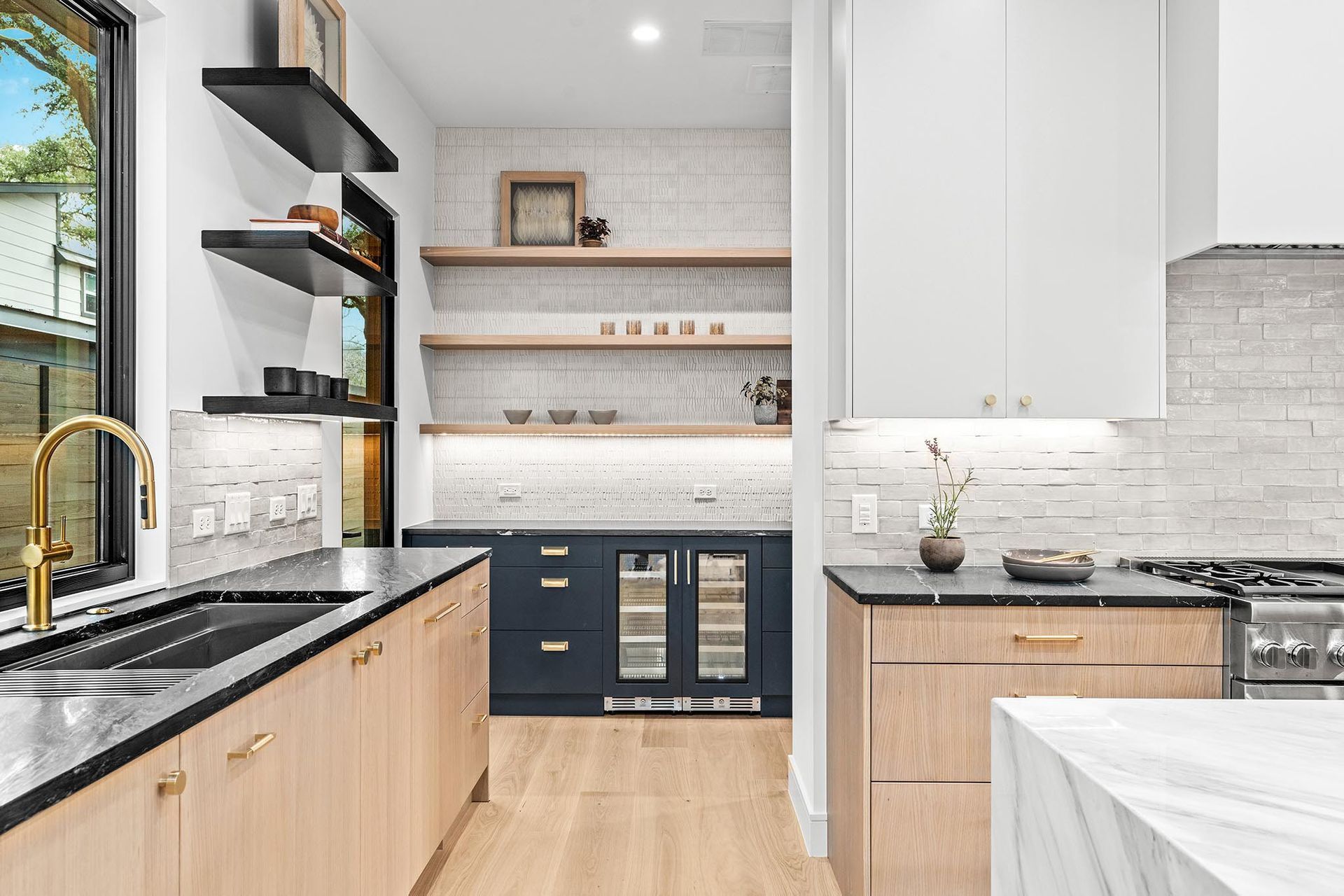 Modern kitchen with light wood cabinets, black countertops, and a dark blue bar area.
