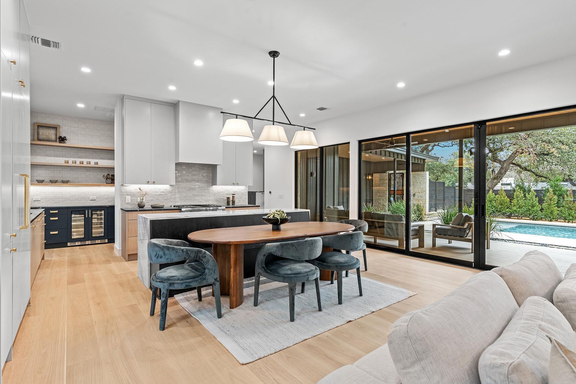 Modern kitchen and dining area with hardwood floors, leading to a backyard with pool.