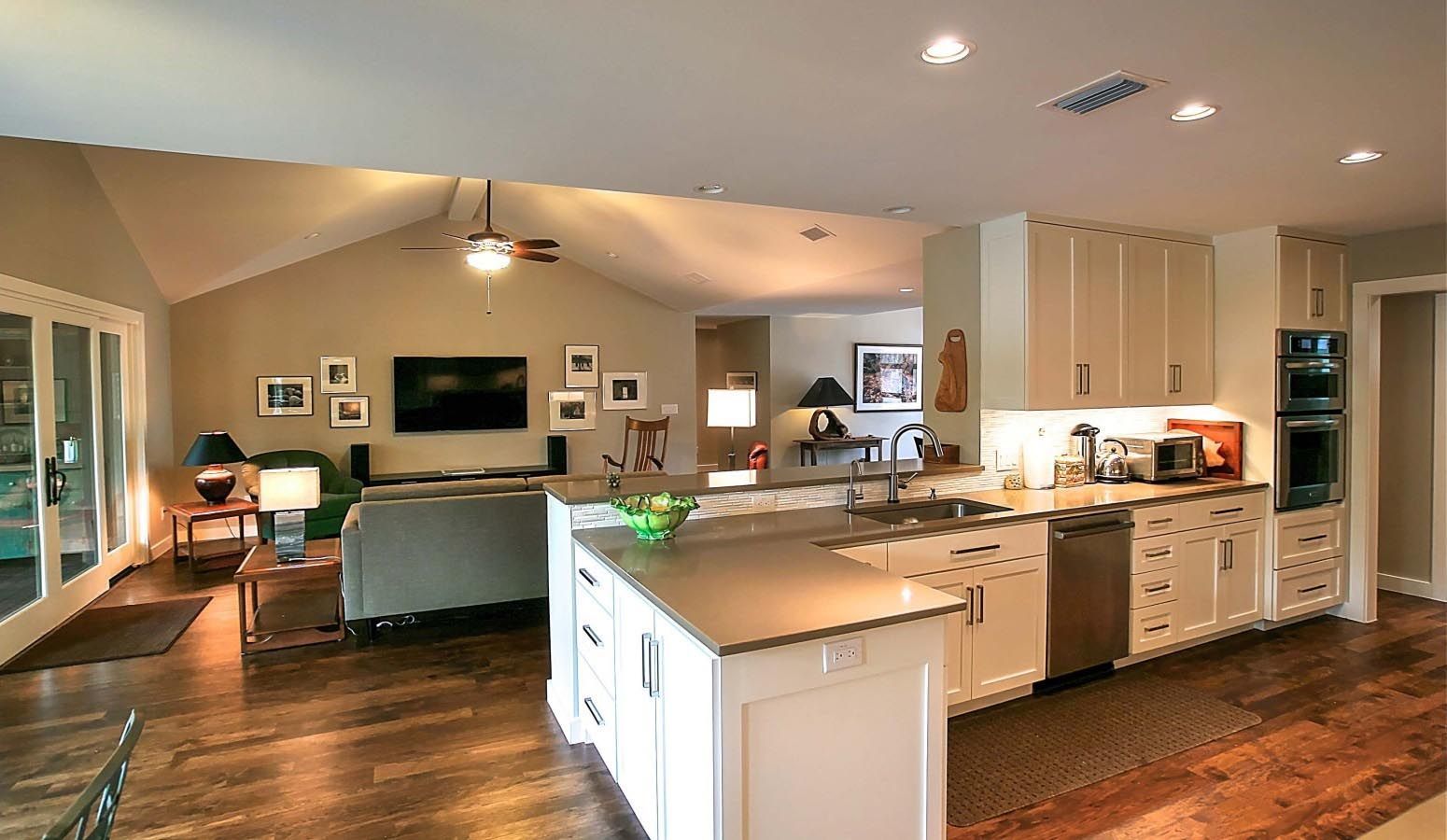 Open-concept kitchen with island, stainless appliances, and view into the living room with a TV and sofa.