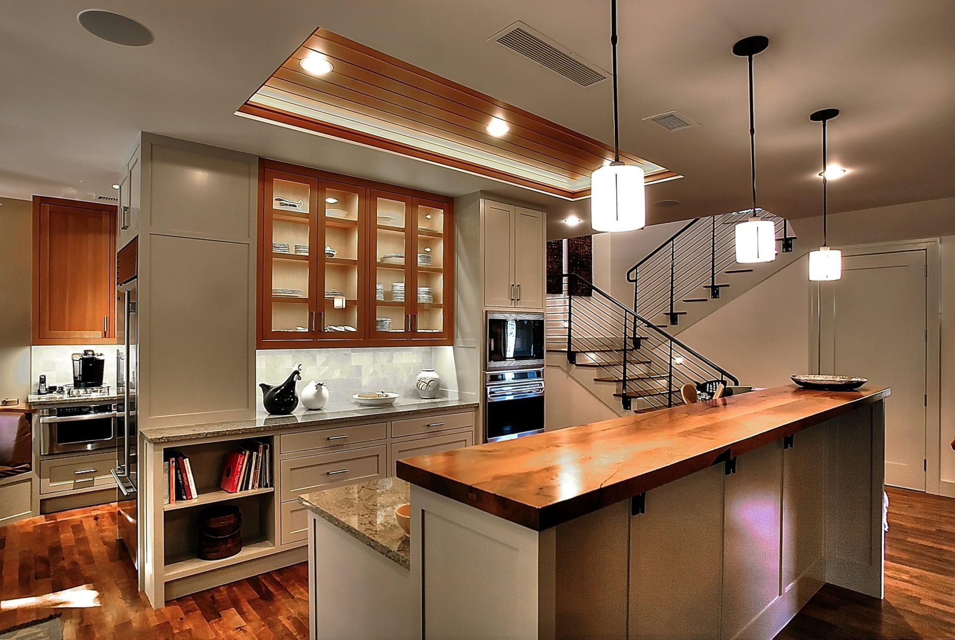 Modern kitchen with wooden island, cabinets, and staircase. Bright lighting.