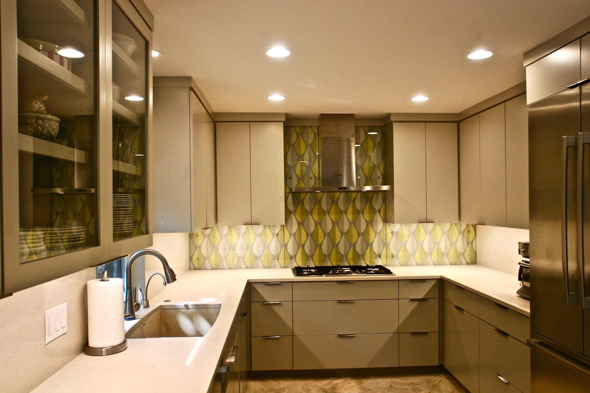 U-shaped modern kitchen with light gray cabinets, stainless steel appliances, and a yellow and green tile backsplash.