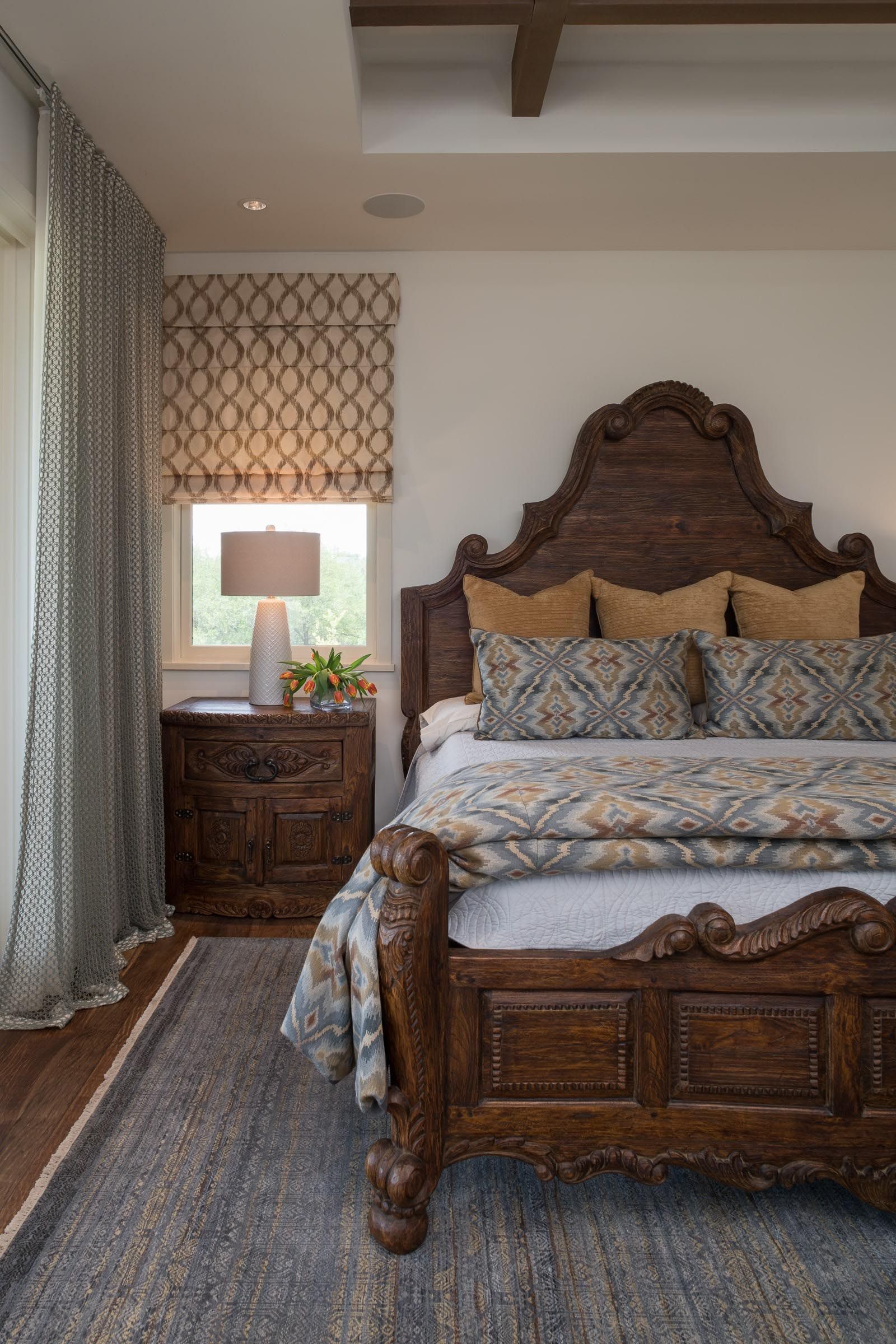 Ornate wood bed in a bedroom with patterned curtains and rug.