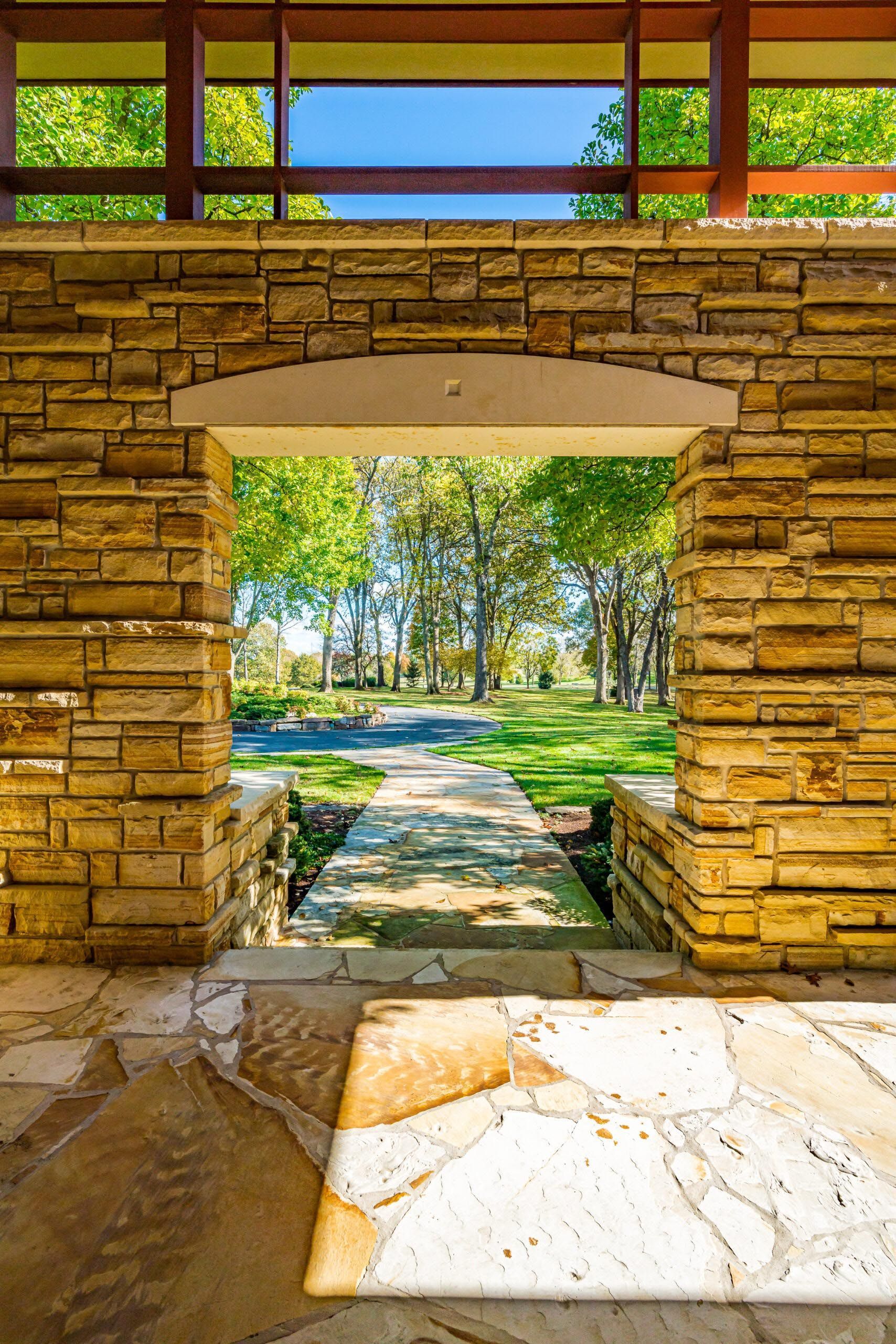 Stone archway leading to a pathway with trees and a blue sky in the background.
