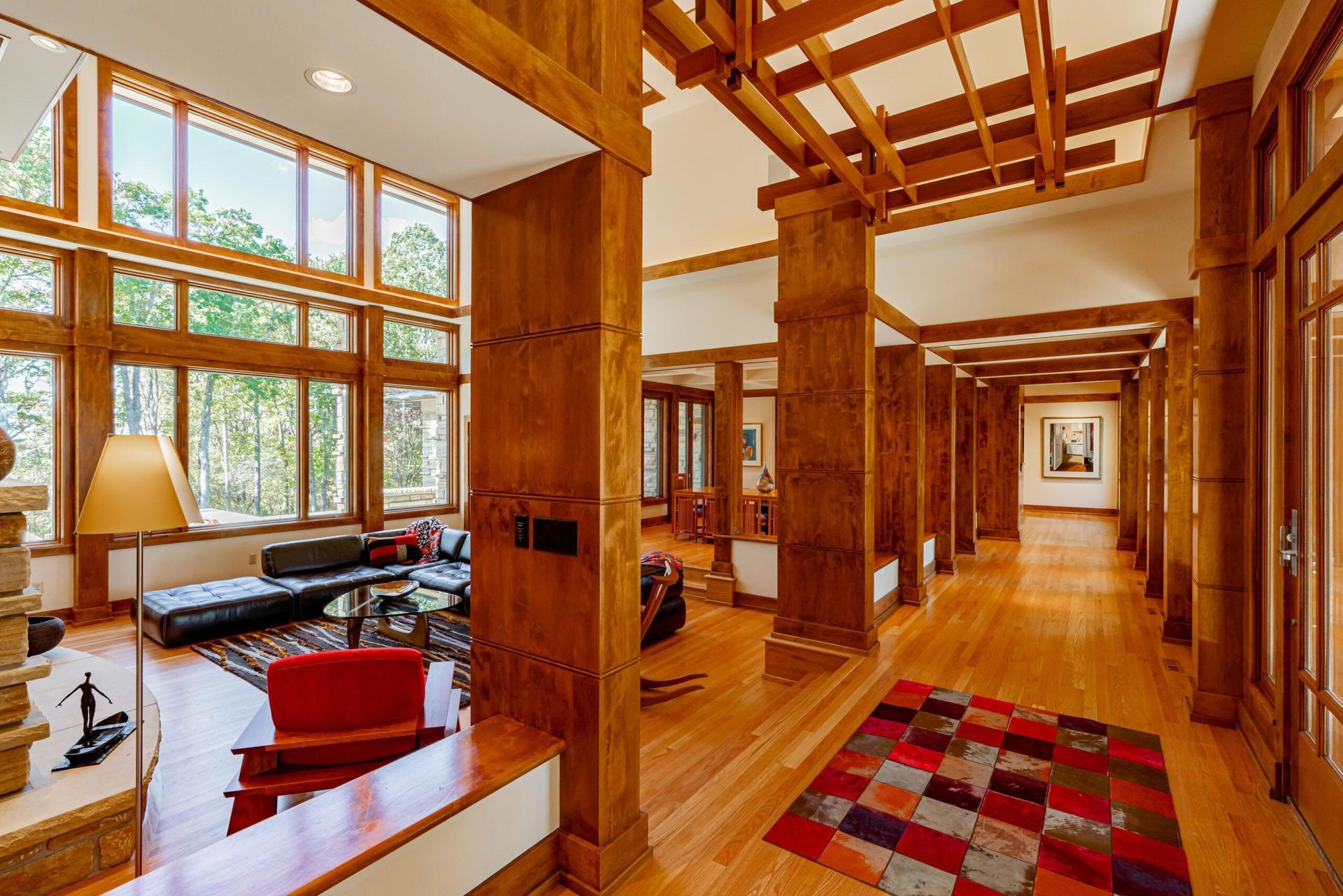 Interior of a wooden home with a hall and living area. Large windows, wood floors, and warm tones.