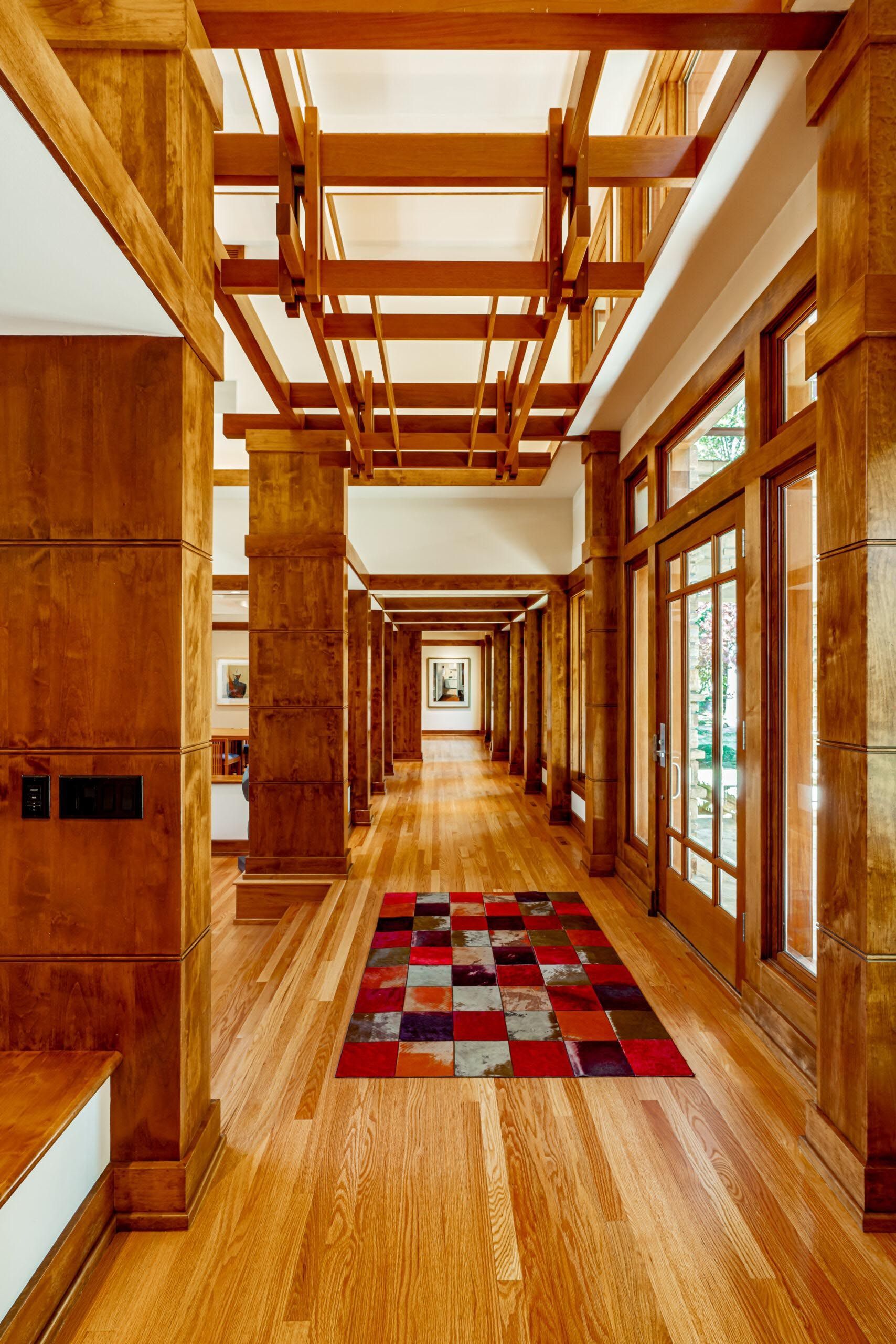 Wooden hallway with columns and geometric rug. Overhead wooden beams and glass doors.
