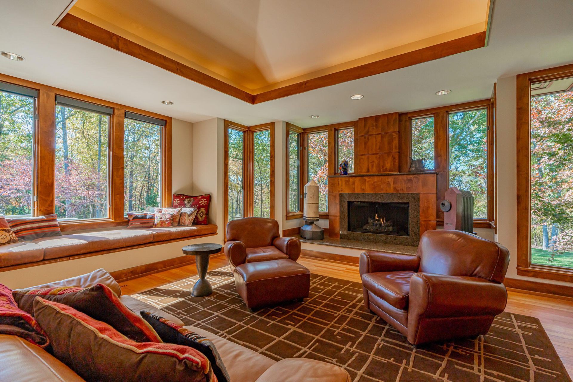Living room with large windows, leather armchairs, a fireplace, and a window seat with forest view.
