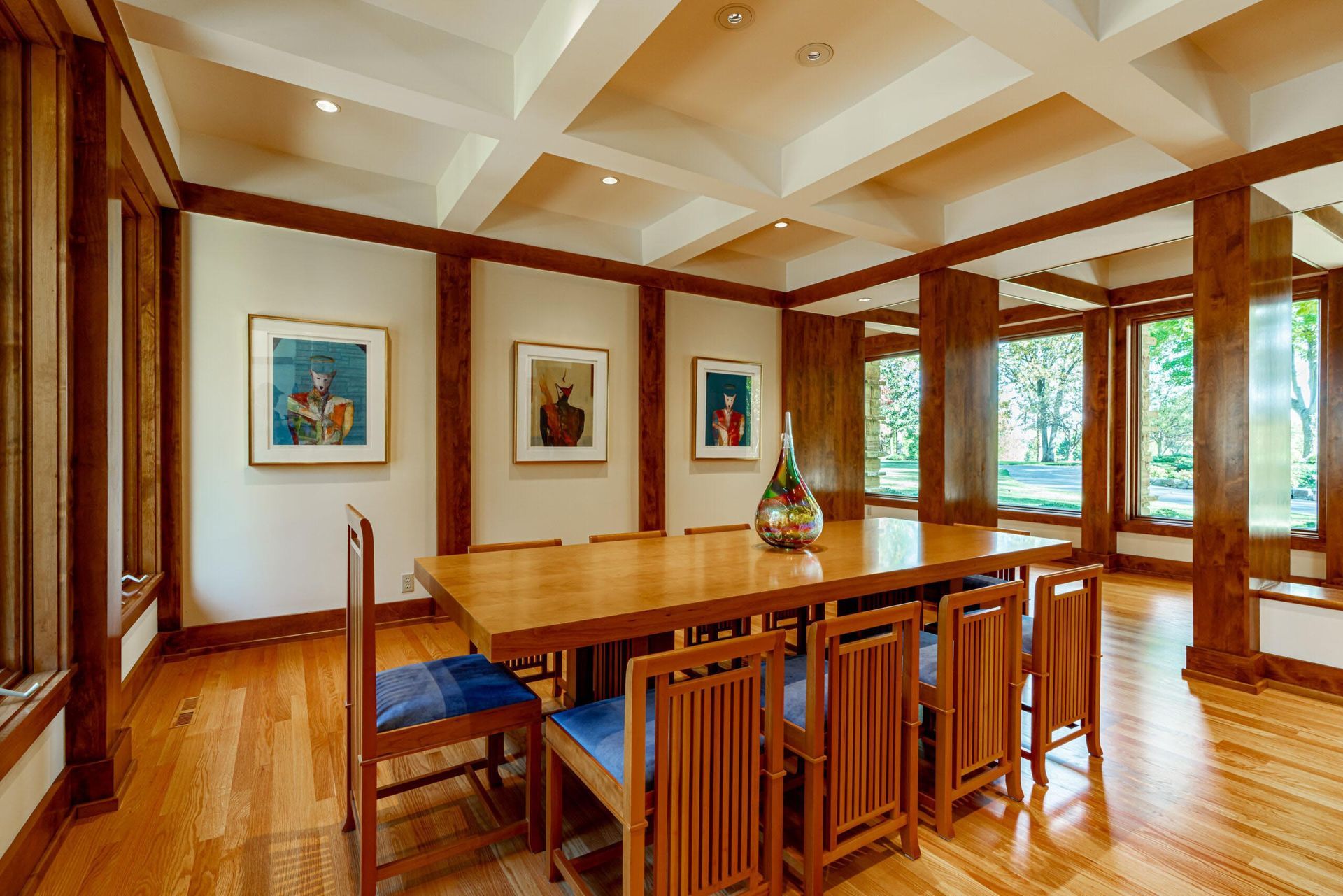 Dining room with wooden table, chairs, art, and windows, featuring light wood floors and dark wood trim.