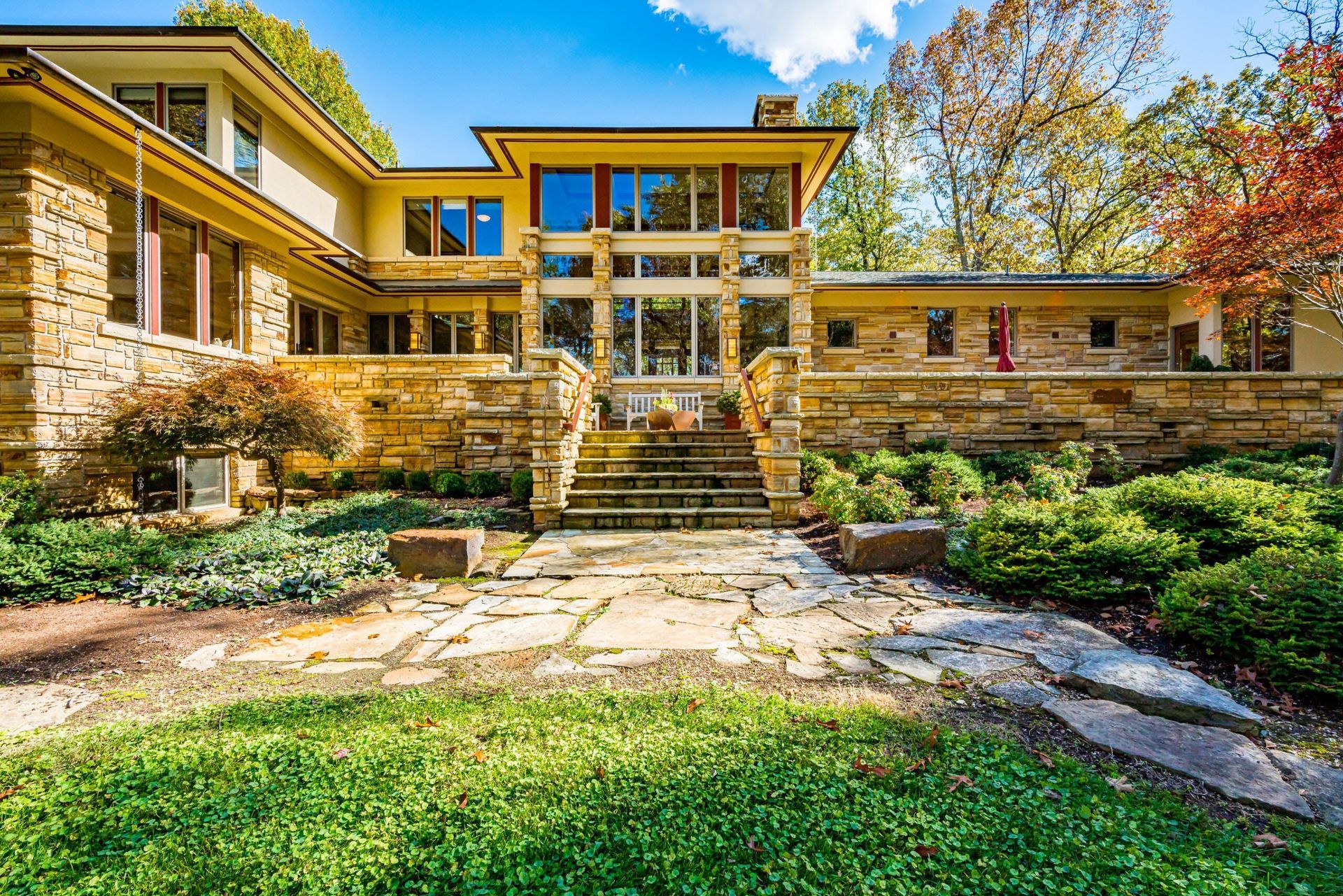 Stone house with glass entrance, steps, and landscaping.