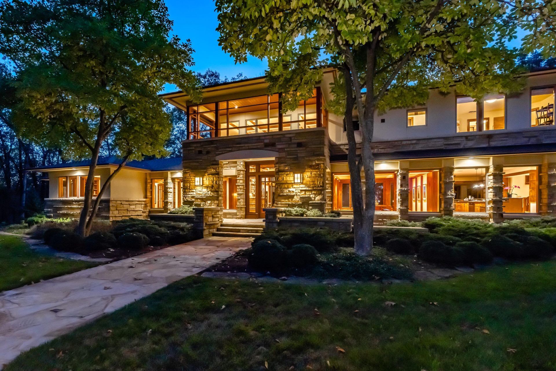 Modern home with stone and wood accents at dusk; walkway leads to illuminated entrance.