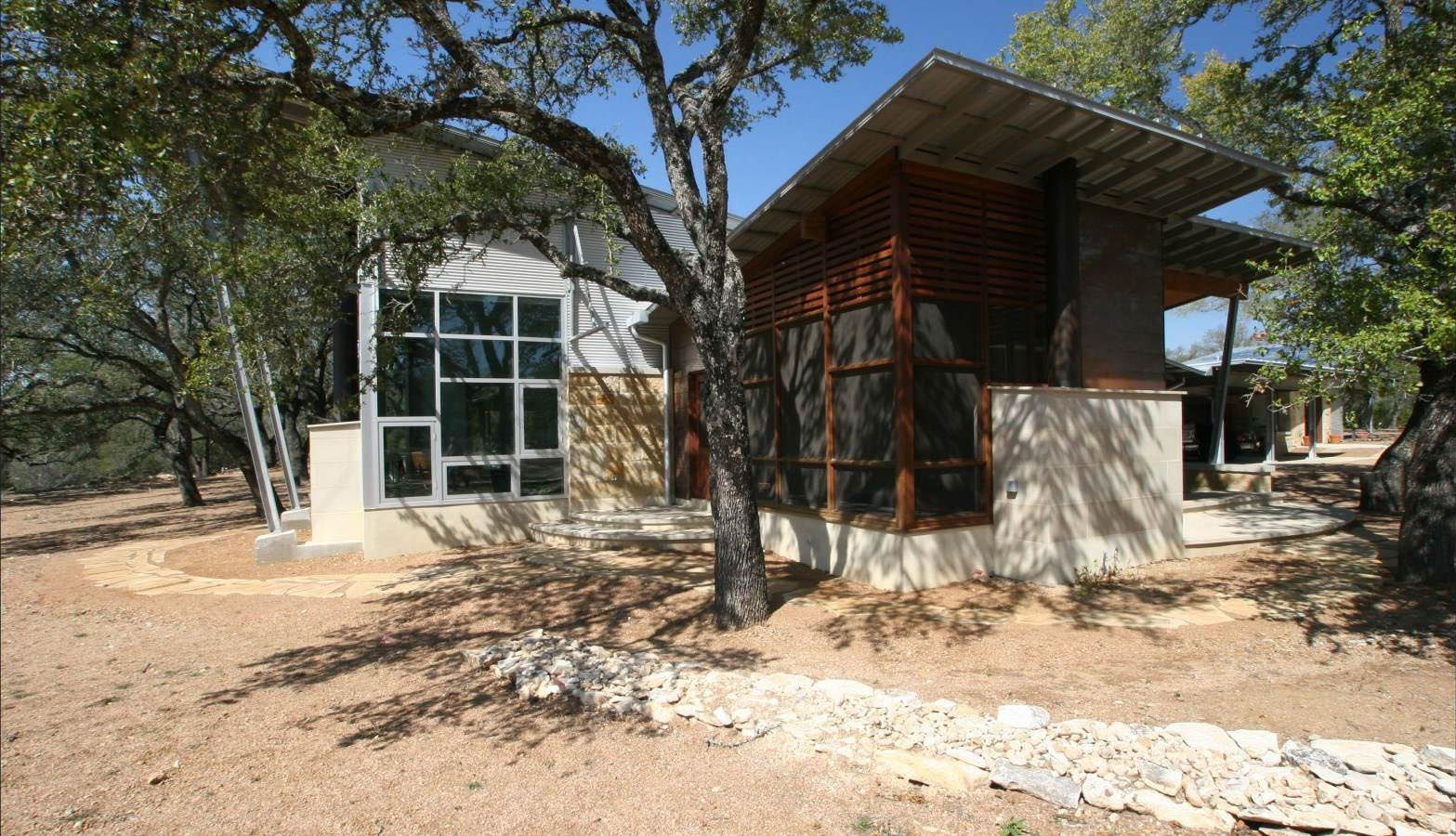 Modern home nestled in a wooded area with large windows, light colored walls, and angled roof.