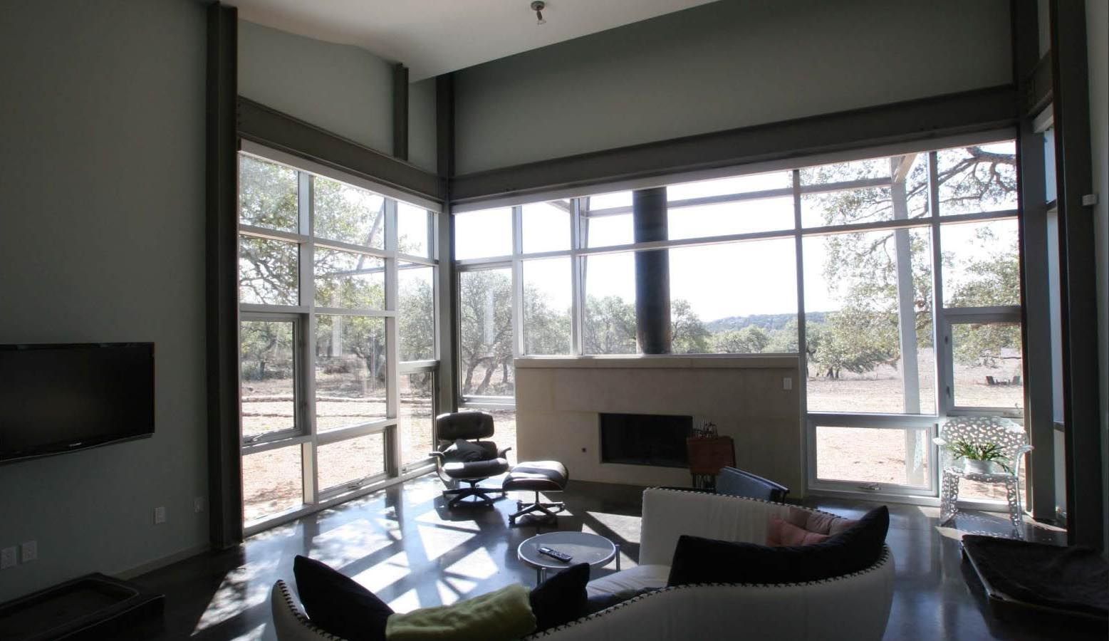 Living room with large windows, fireplace, modern furniture, and a view of trees.