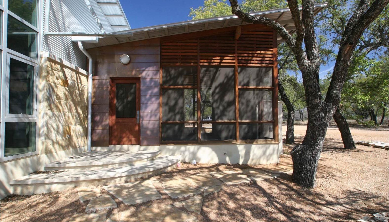 Exterior of a building with a screened porch, brown door, and stone pathway under blue sky.