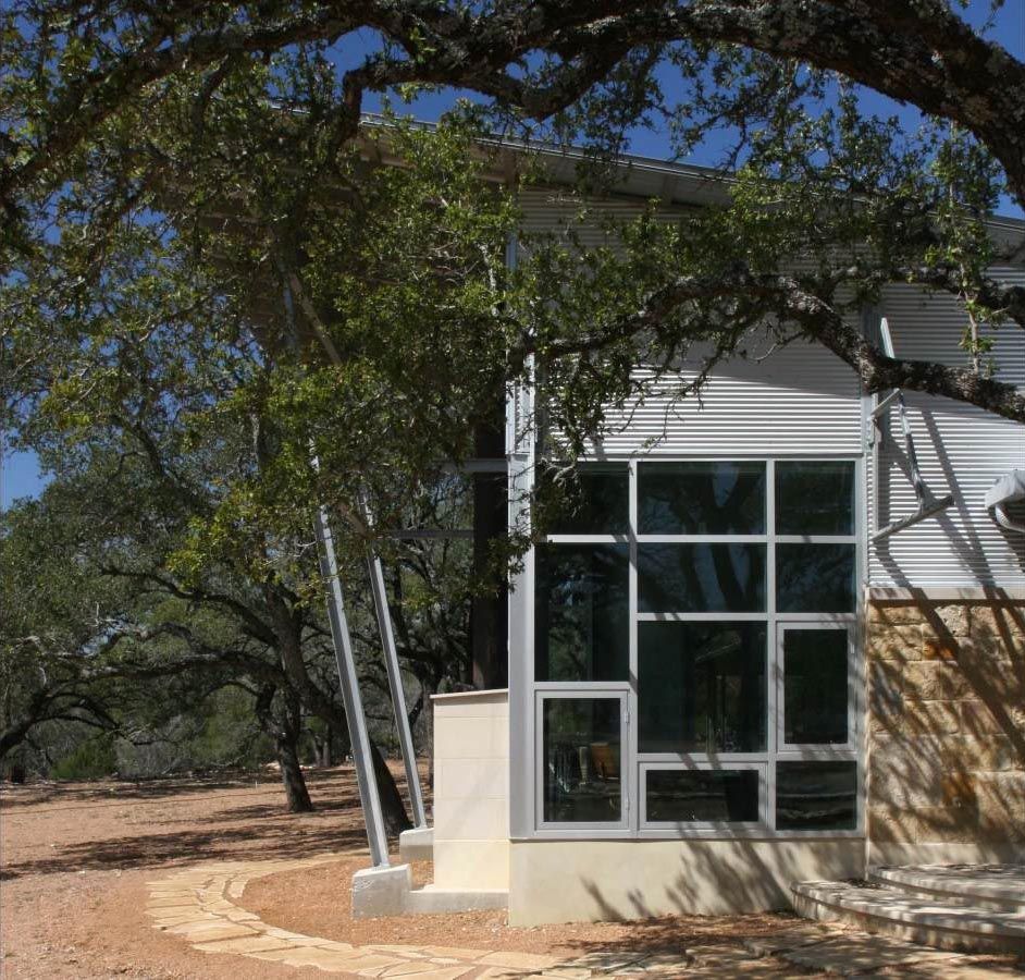 Modern building with large windows, set amidst trees and a gravel pathway.