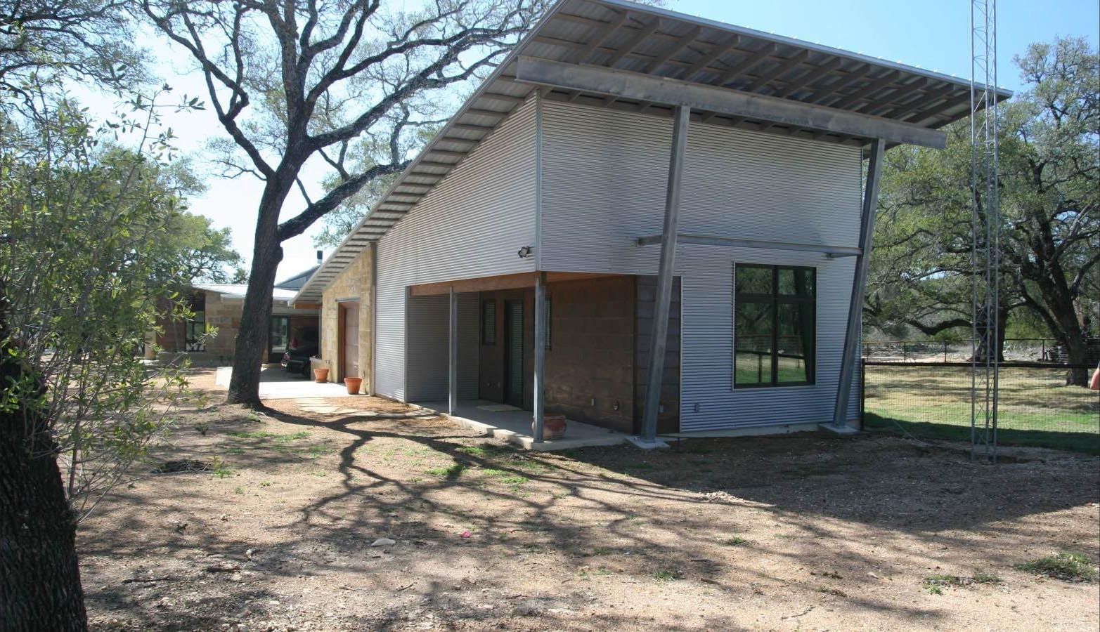 Modern house with a corrugated metal roof and siding, set in a dry, wooded landscape.